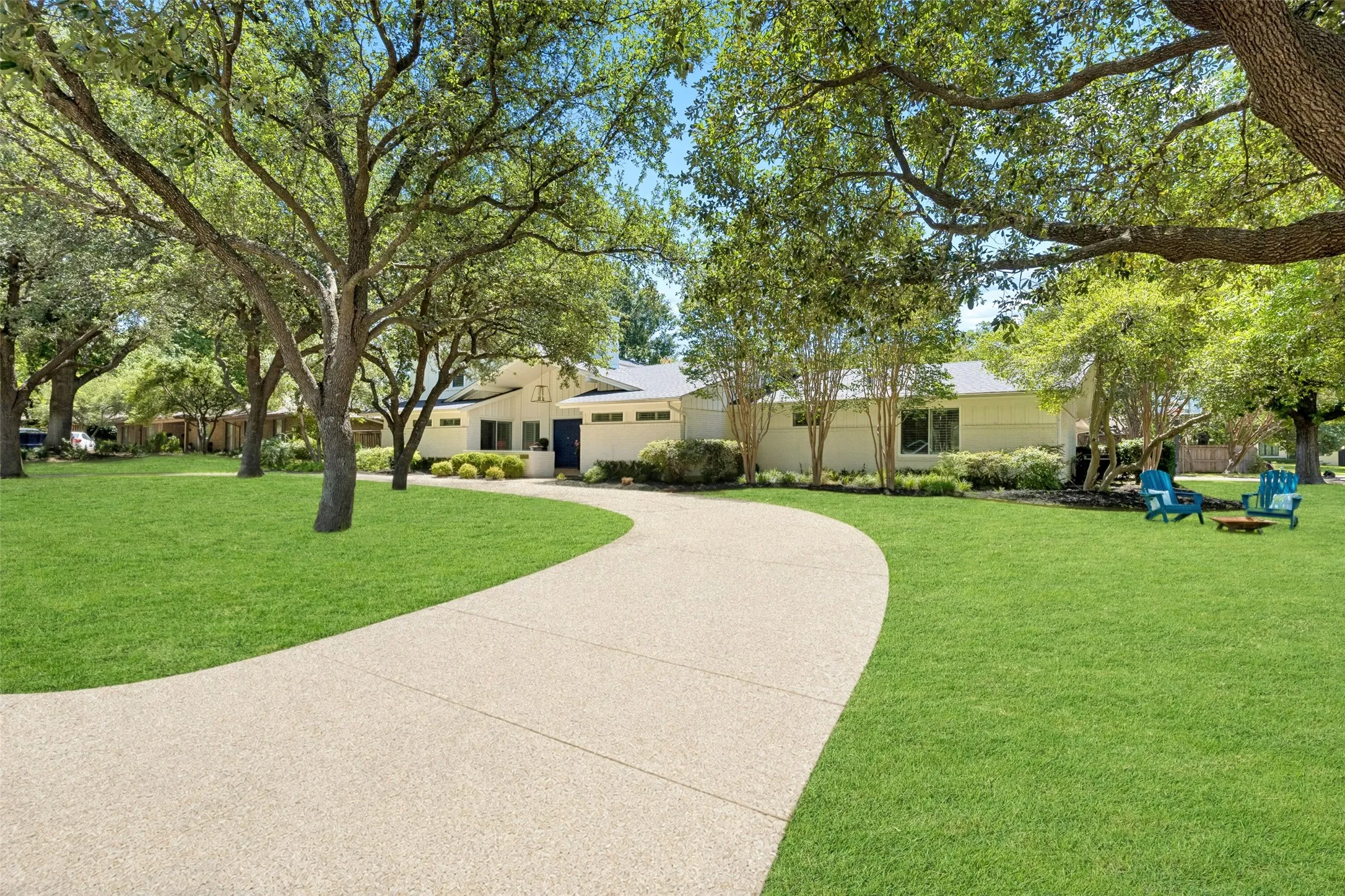 A sweeping circular drive winds beneath mature trees, creating an inviting approach to this beautifully landscaped home.