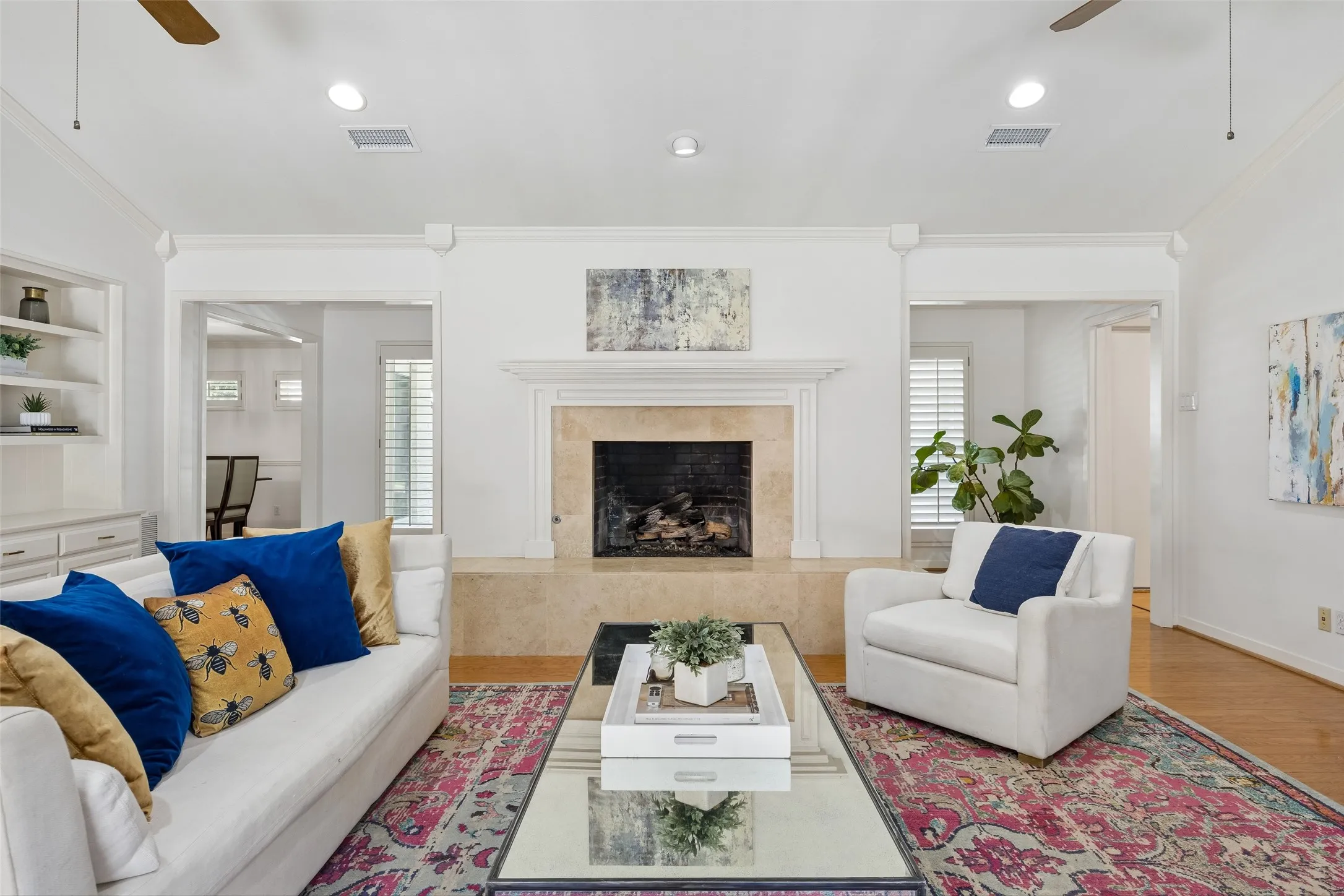 Located in the center of the home. The living room is anchored by a classic fireplace and features built-in shelving, wood floors, and a bright, open feel.
