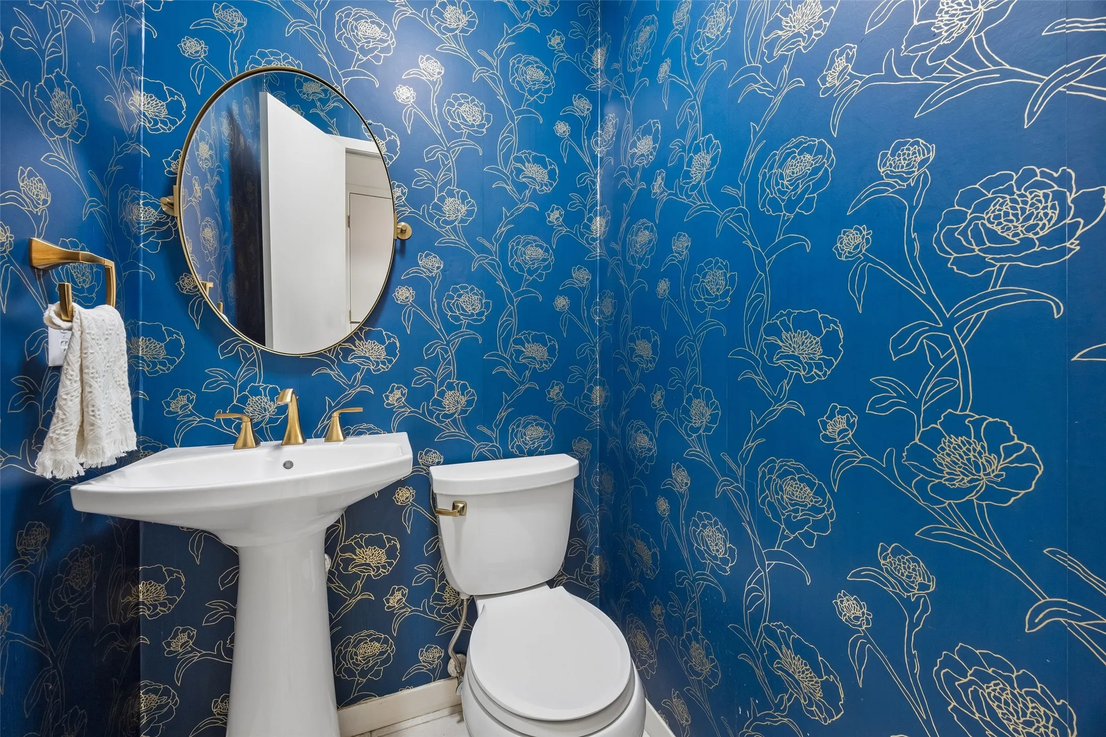 A stylish powder bath makes a bold statement with vibrant floral wallcovering and warm brass accents.