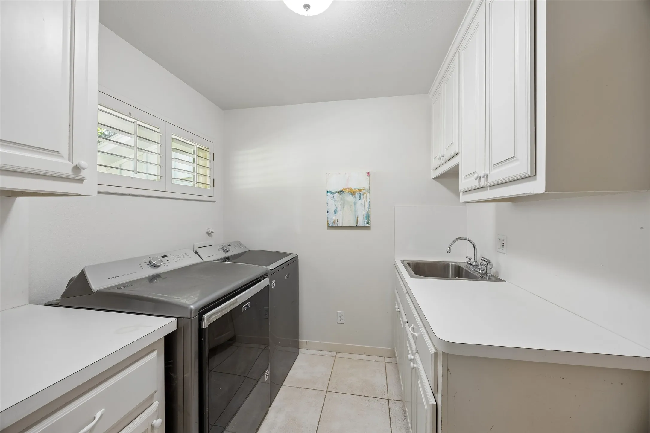 A spacious laundry room offers abundant cabinetry, generous counter space, a utility sink, and natural light.