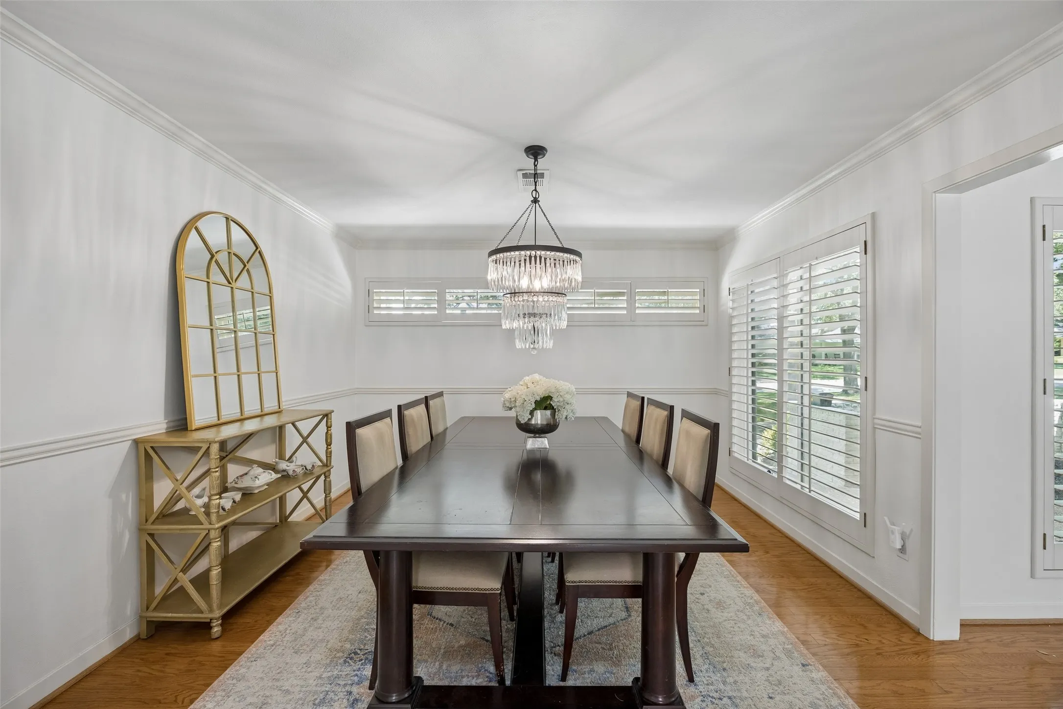 Formal dining room featuring wood flooring, plantation shutters, elegant millwork and a striking statement chandelier.