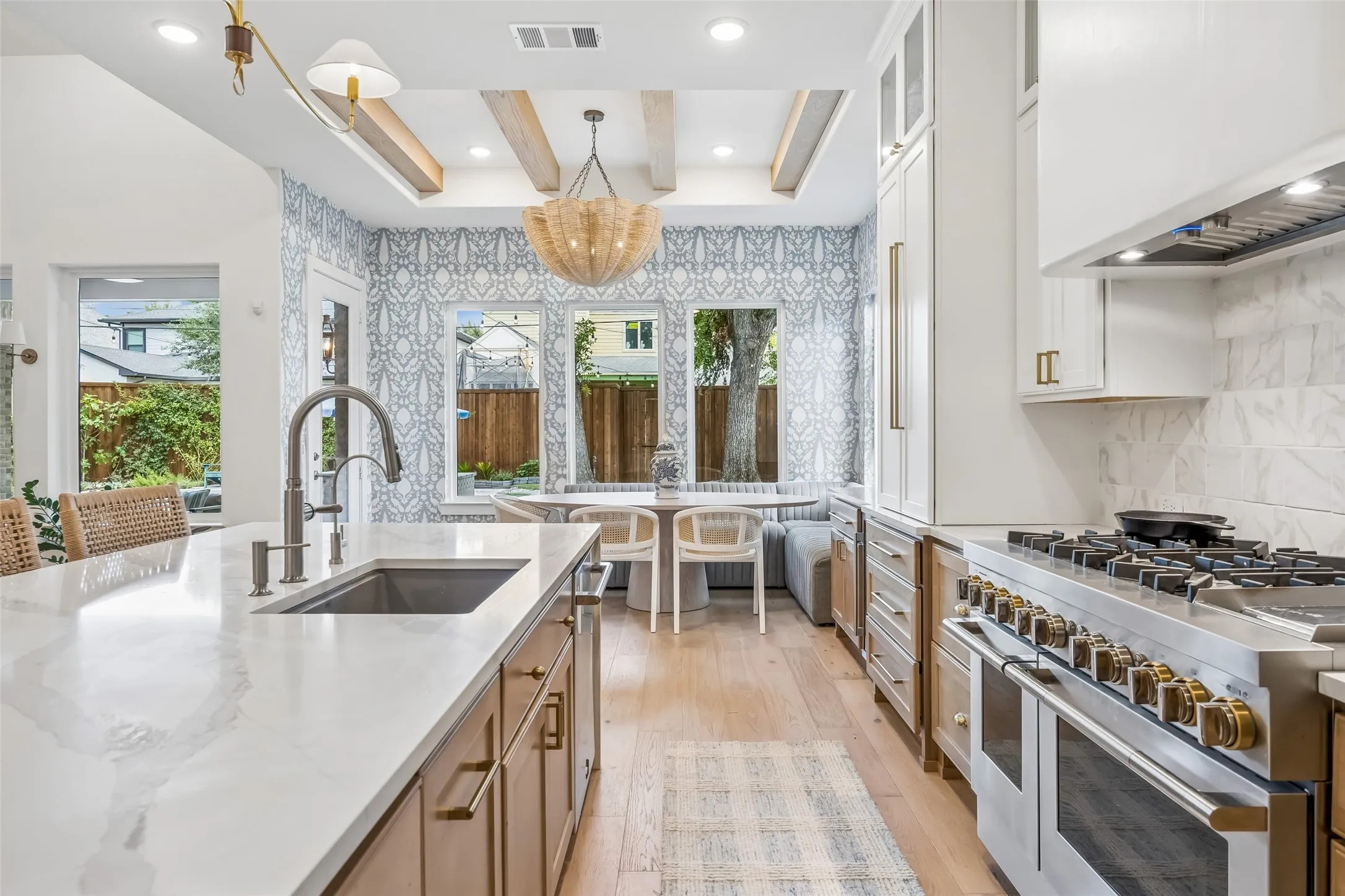 A beautifully curated kitchen opens to the breakfast nook, pairing warm custom cabinetry and expansive stone surfaces with professional-grade appliances, brass accents and designer details throughout.