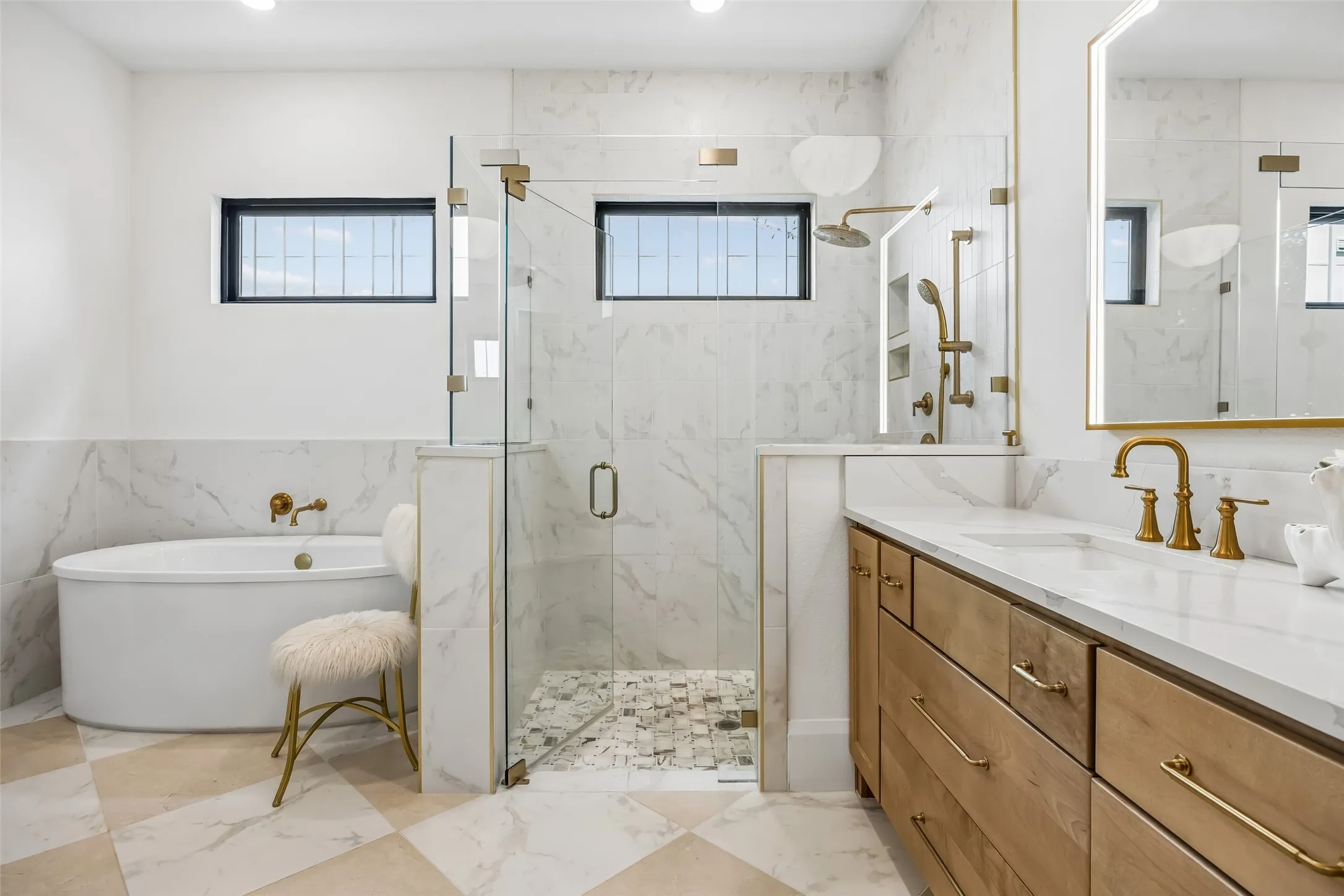 A beautifully appointed primary bath features a freestanding soaking tub, oversized glass-enclosed shower, warm wood vanity, brass fixtures and striking tile for a polished, spa-like feel.