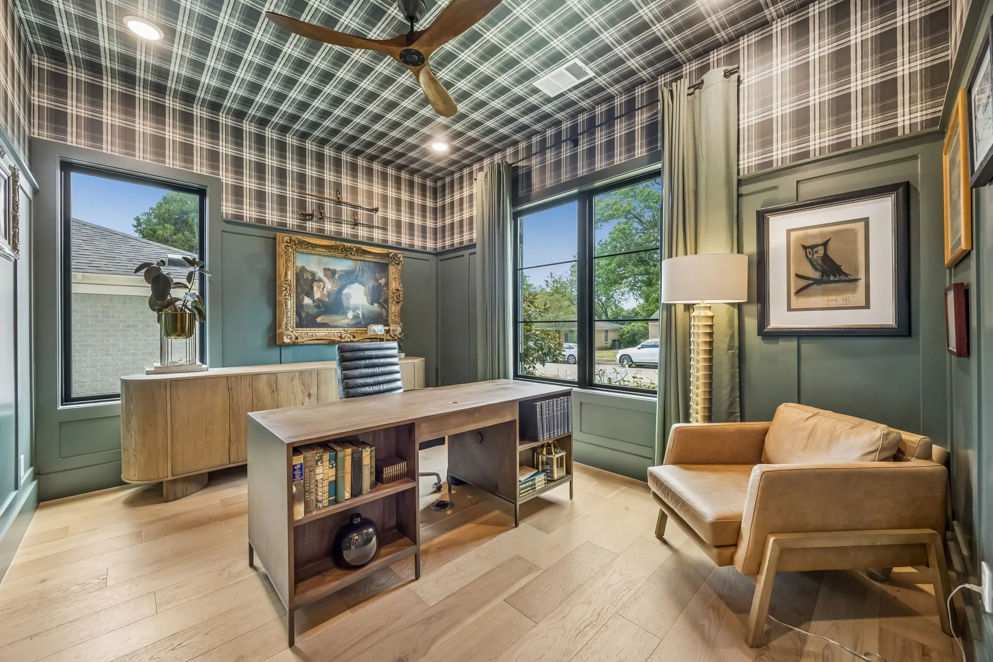 A dramatic home office makes a bold design statement with rich paneled walls, plaid wallcovering extending across the ceiling, wood floors and abundant natural light.