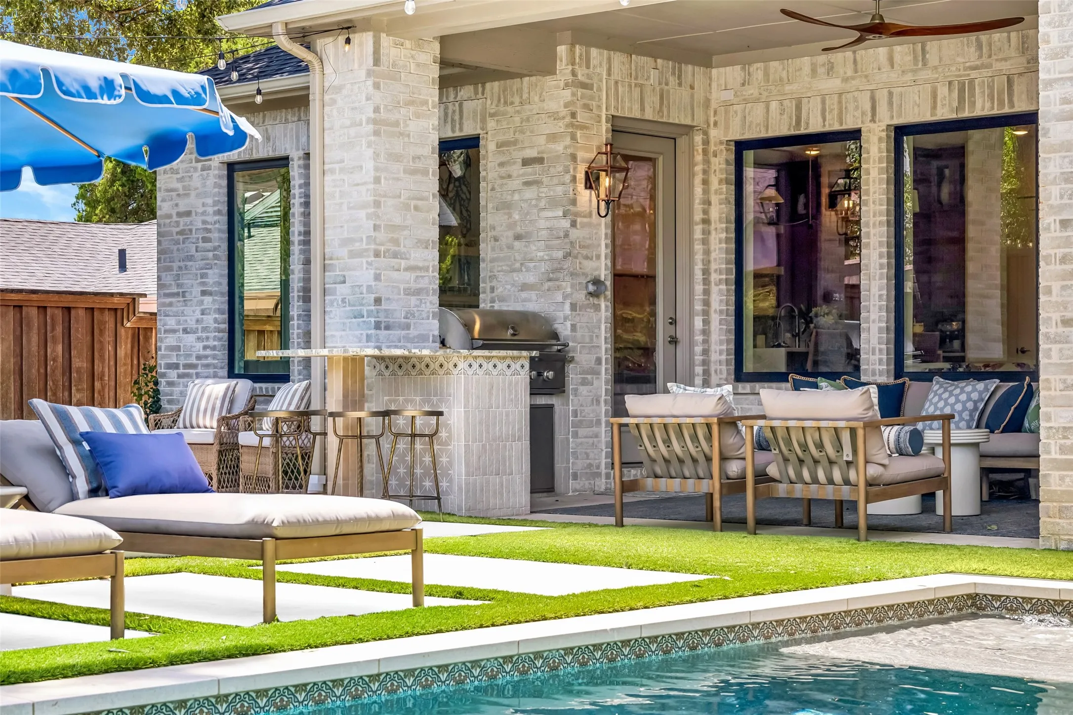 A covered outdoor living area overlooks the pool and features a built-in grill, decorative tilework, ceiling fan and ample space for relaxing and entertaining.