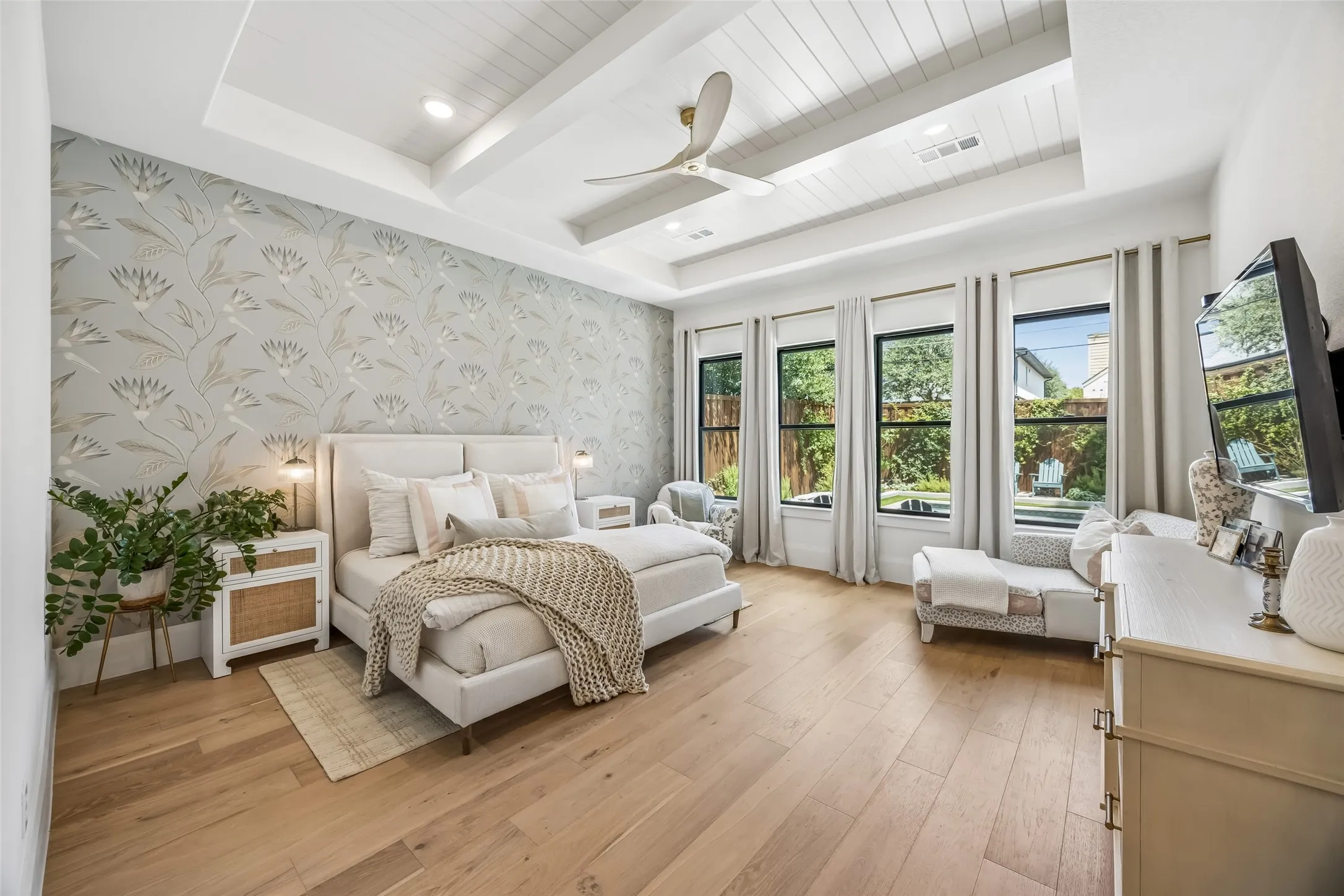 A serene primary suite features a vaulted ceiling, designer wallcovering and abundant natural light from a wall of windows overlooking the backyard.