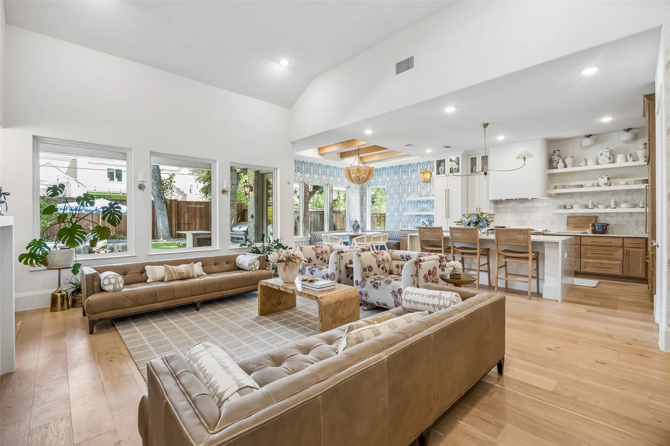 A light-filled living area showcases soaring ceilings, wood floors and an open-concept design that flows seamlessly into the kitchen and breakfast nook, with walls of windows overlooking the backyard.