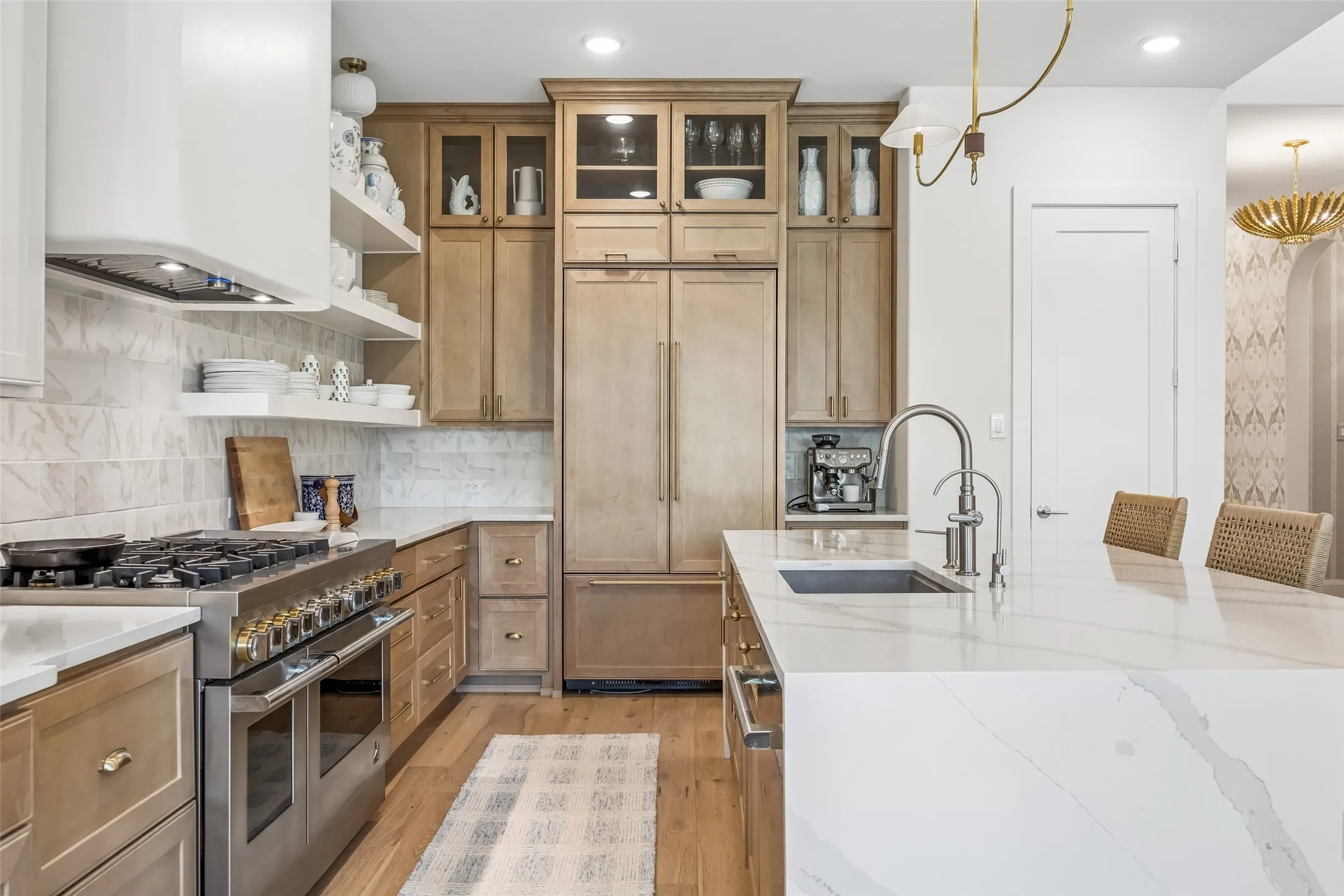 A designer kitchen pairs warm custom cabinetry with striking stone surfaces, open shelving, professional-grade appliances and brass accents for a sophisticated, highly functional space.