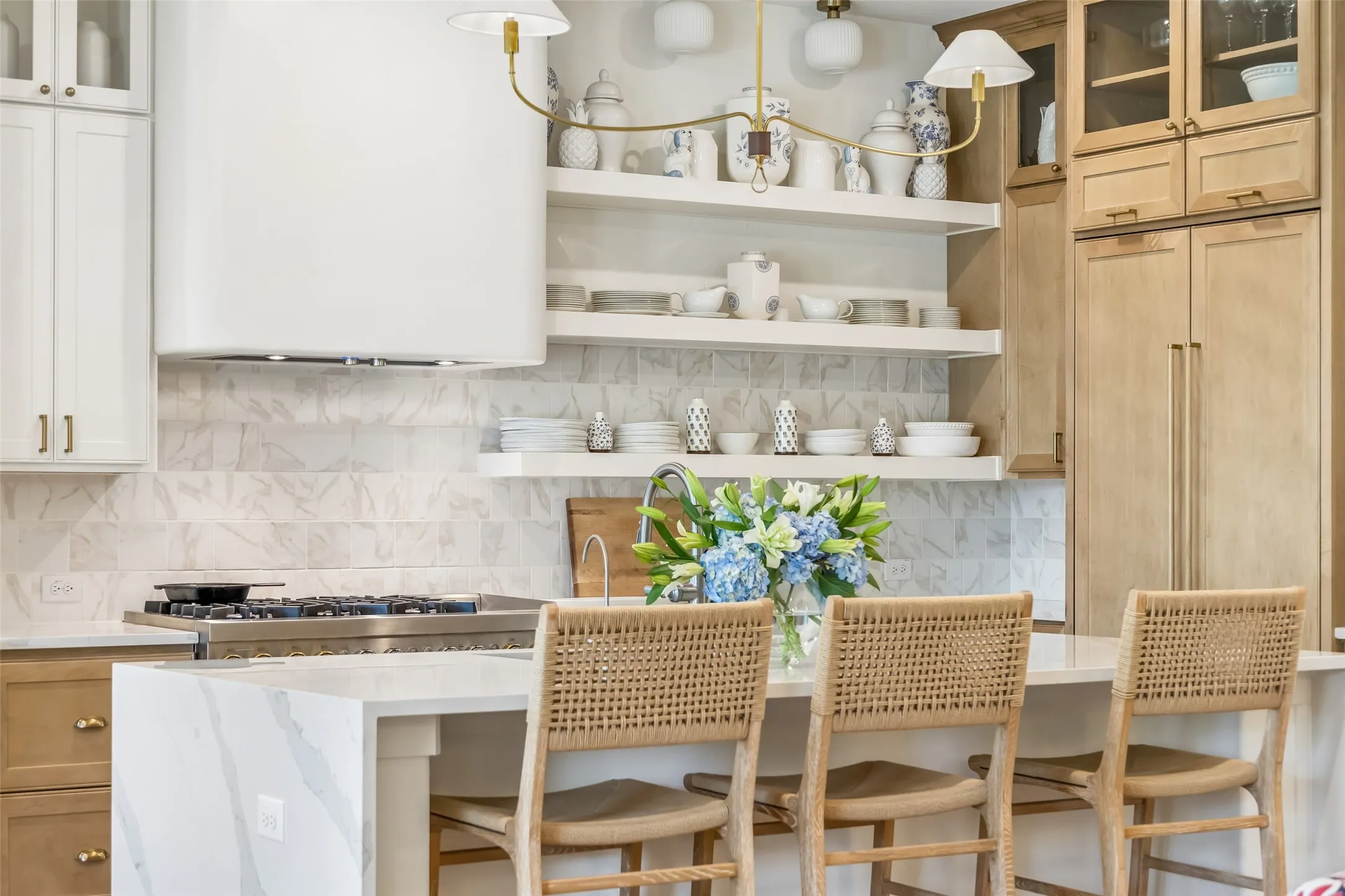 A closer look at the designer kitchen highlights the striking waterfall-edge island, open shelving, mixed custom cabinetry, brass accents and beautifully layered finishes.
