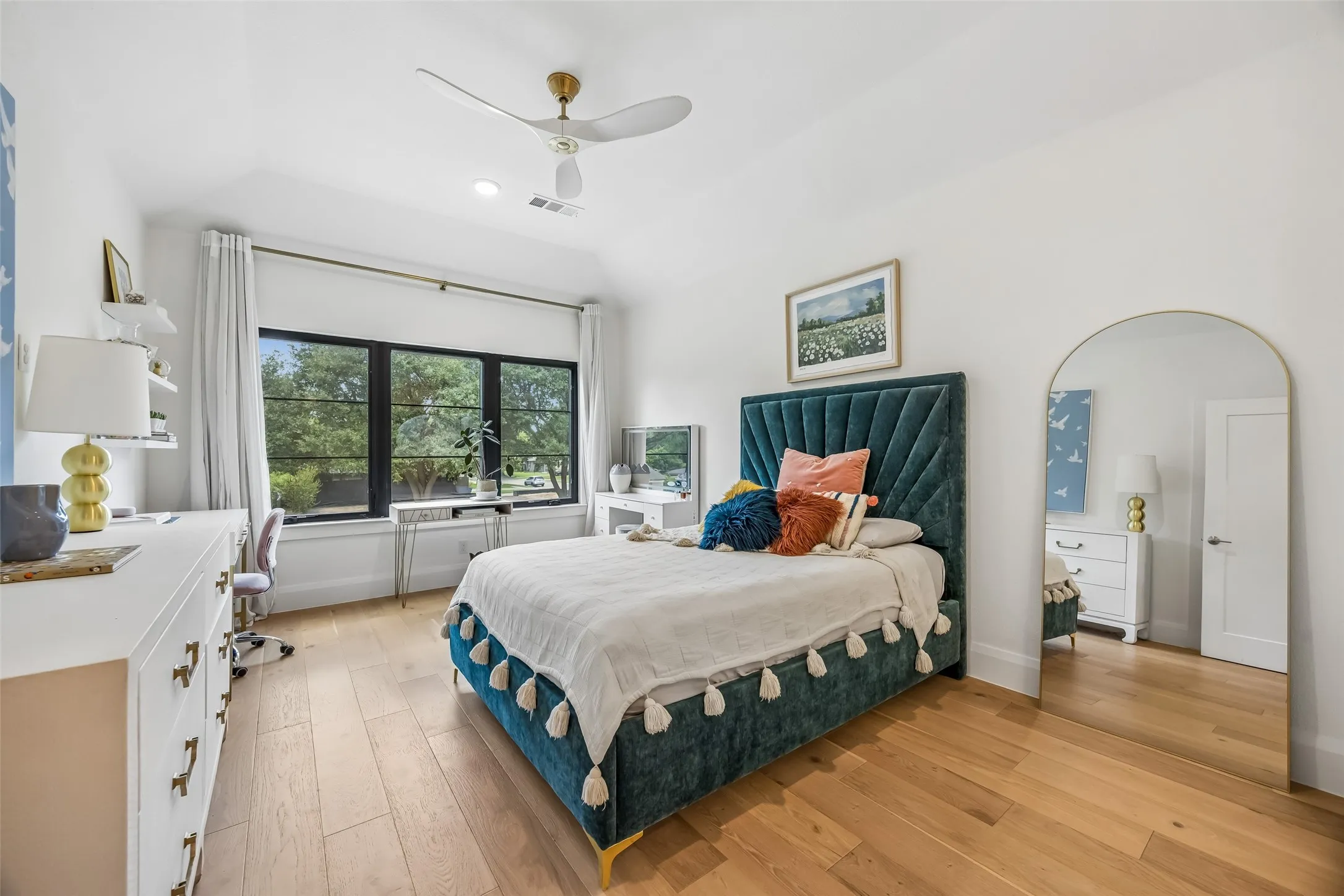 A bright upstairs bedroom features wood floors, a vaulted ceiling and a large window that fills the space with natural light.