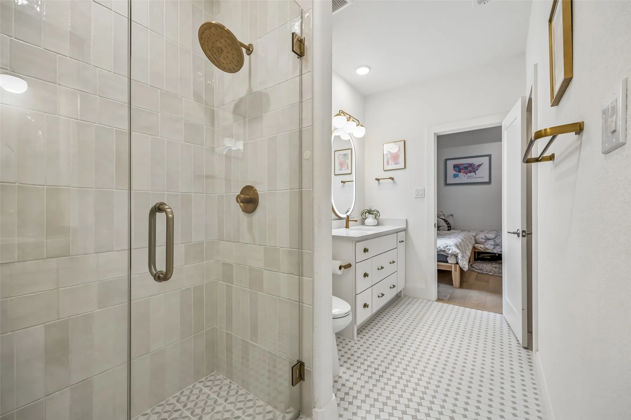 A beautifully finished upstairs bath features a glass-enclosed shower, designer tile, brass fixtures and a crisp vanity with thoughtful custom details.