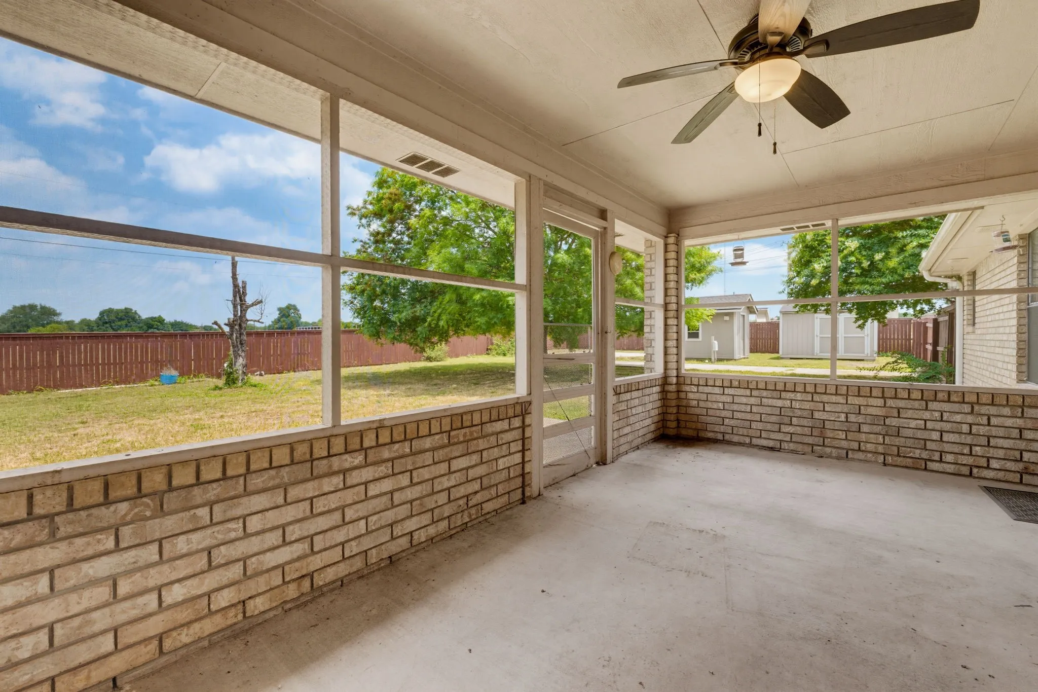 Screened porch featuring a ceiling fan, brick half-wall, and concrete flooring