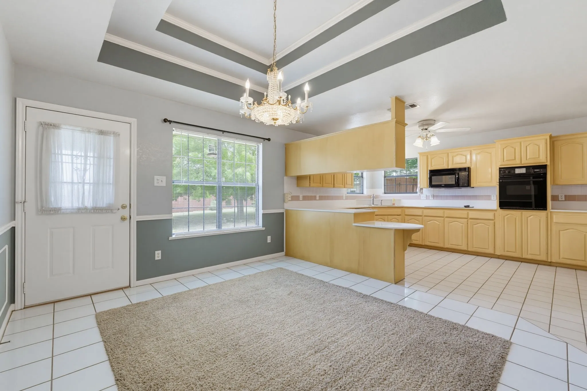 Tray ceiling with decorative trim, chandelier lighting, and a kitchen with extensive cabinetry, built-in appliances, and a breakfast bar