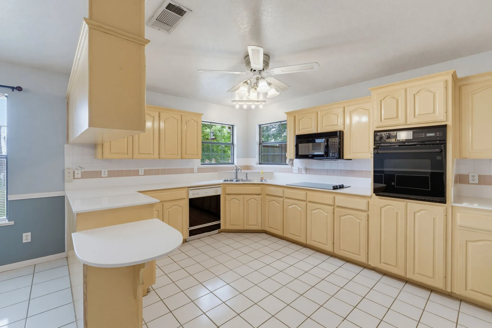 Kitchen featuring extensive cabinetry, tile flooring, built-in wall oven, built-in microwave, and a ceiling fan