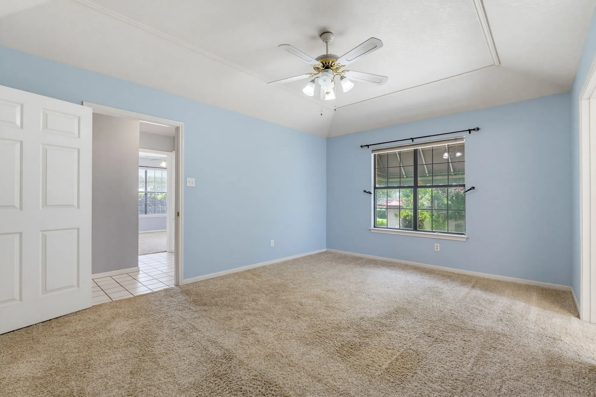 Vaulted ceiling with a ceiling fan, carpet flooring, a large window, and an open doorway