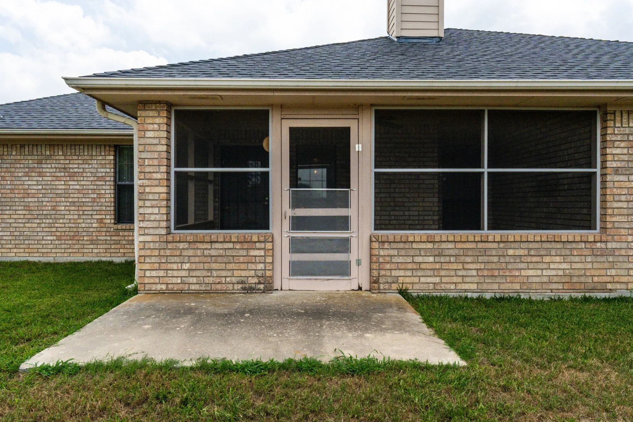 Brick exterior with a screened-in patio and a concrete pad