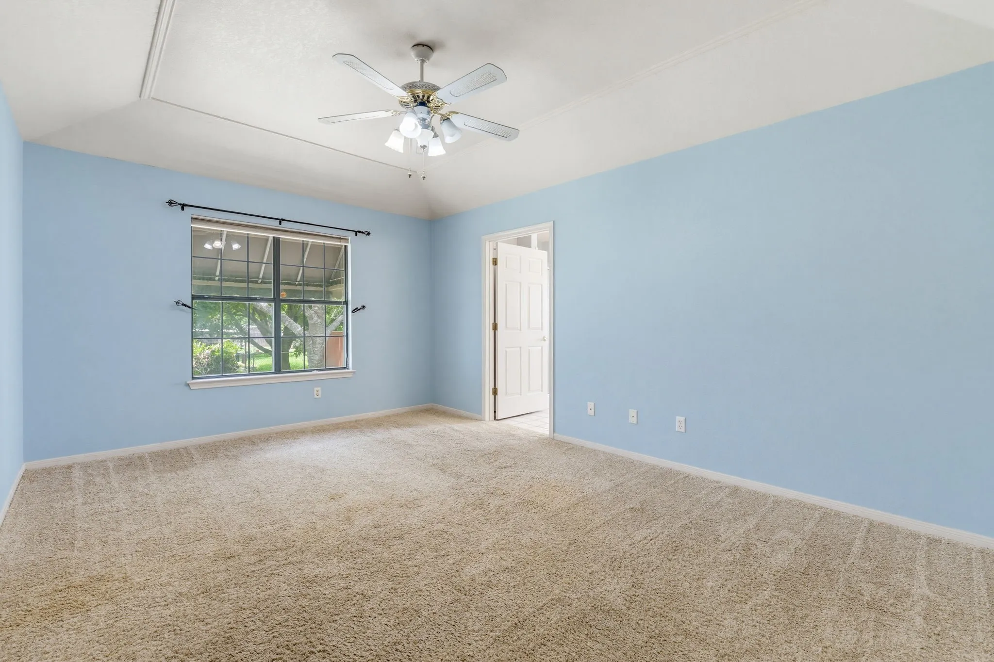 Tray ceiling, ceiling fan, carpeting, window with outdoor scenery, and a white interior door