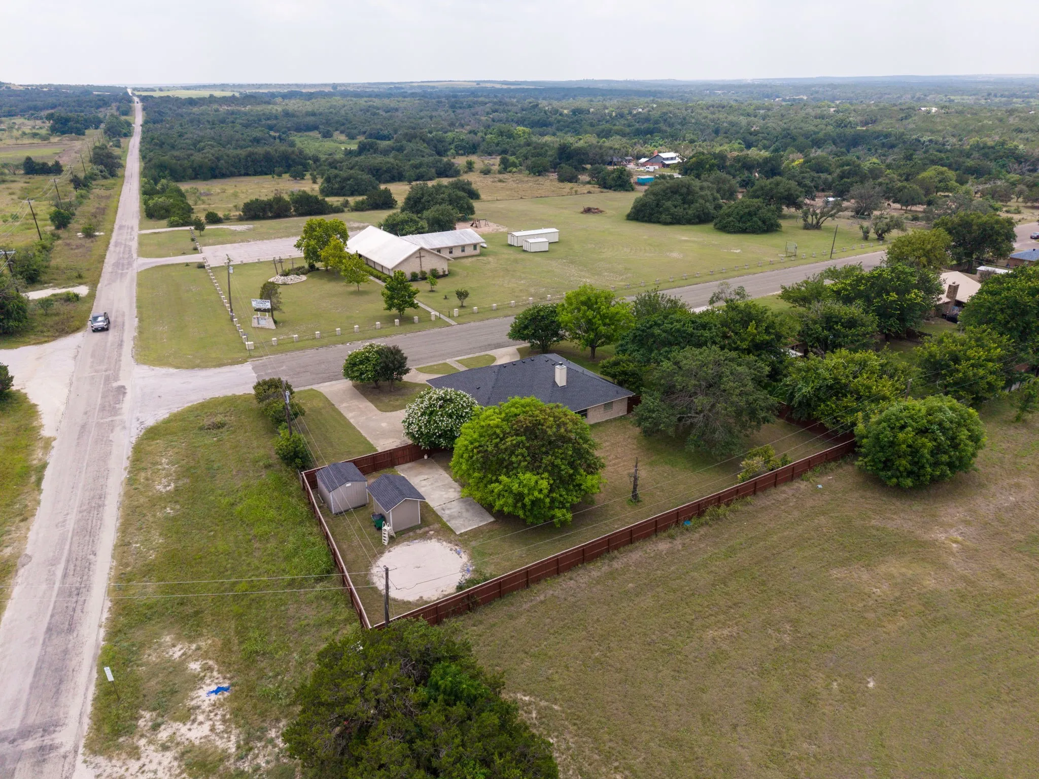 Fenced backyard with mature trees, two storage sheds, and a circular gravel area