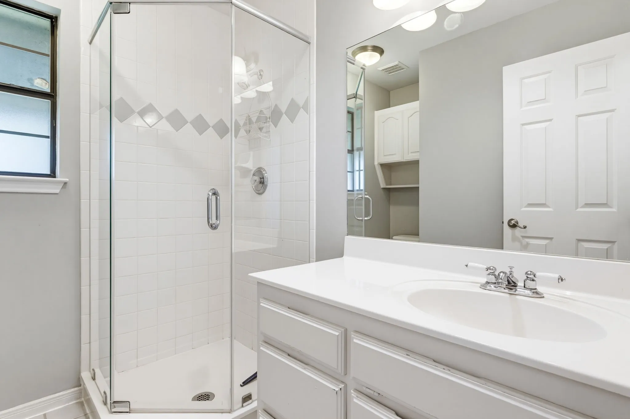 Glass-enclosed shower with white tiled walls and diamond accent border