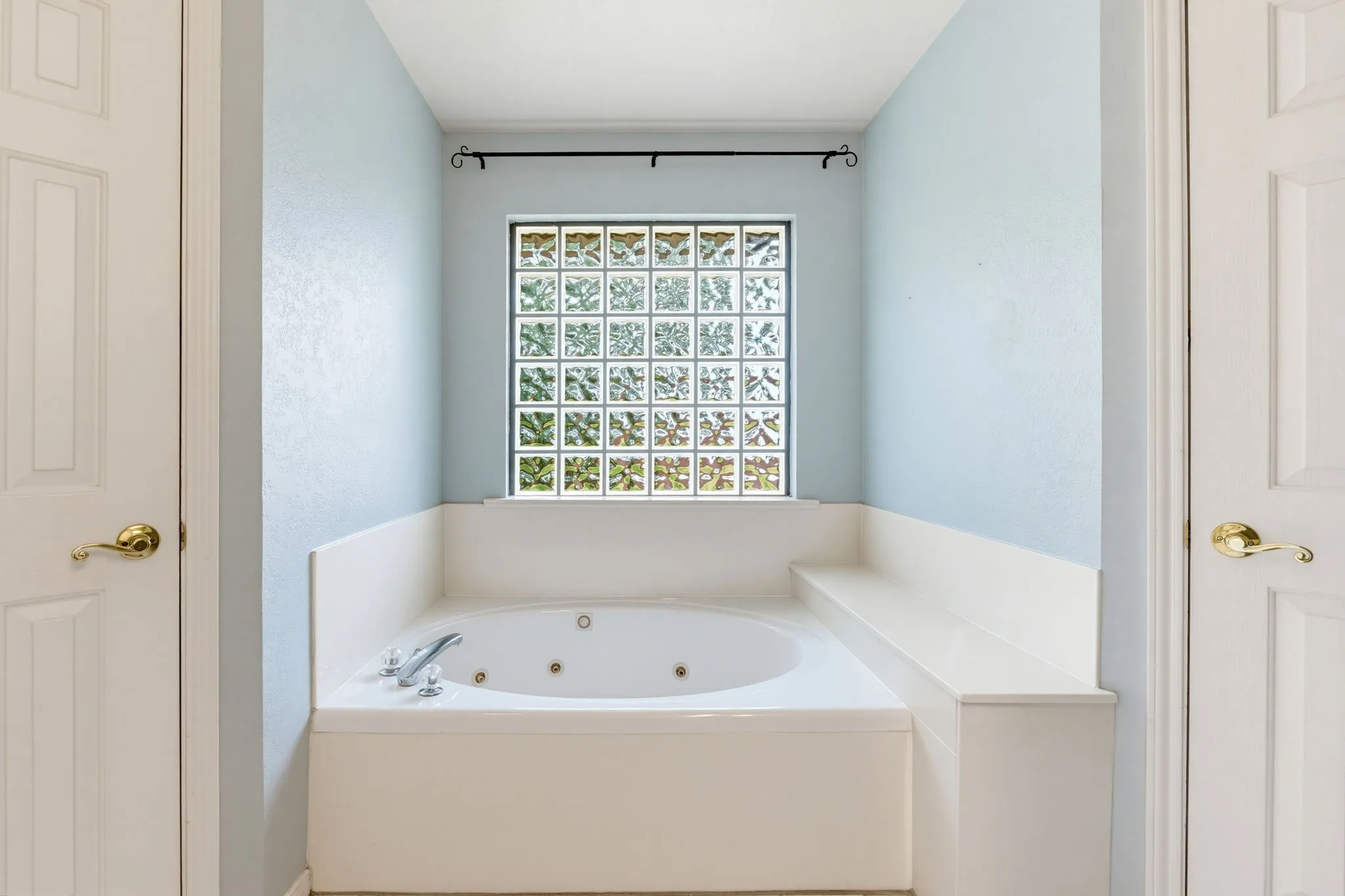 Built-in jetted tub with chrome fixtures, glass block window, and light blue wall finish