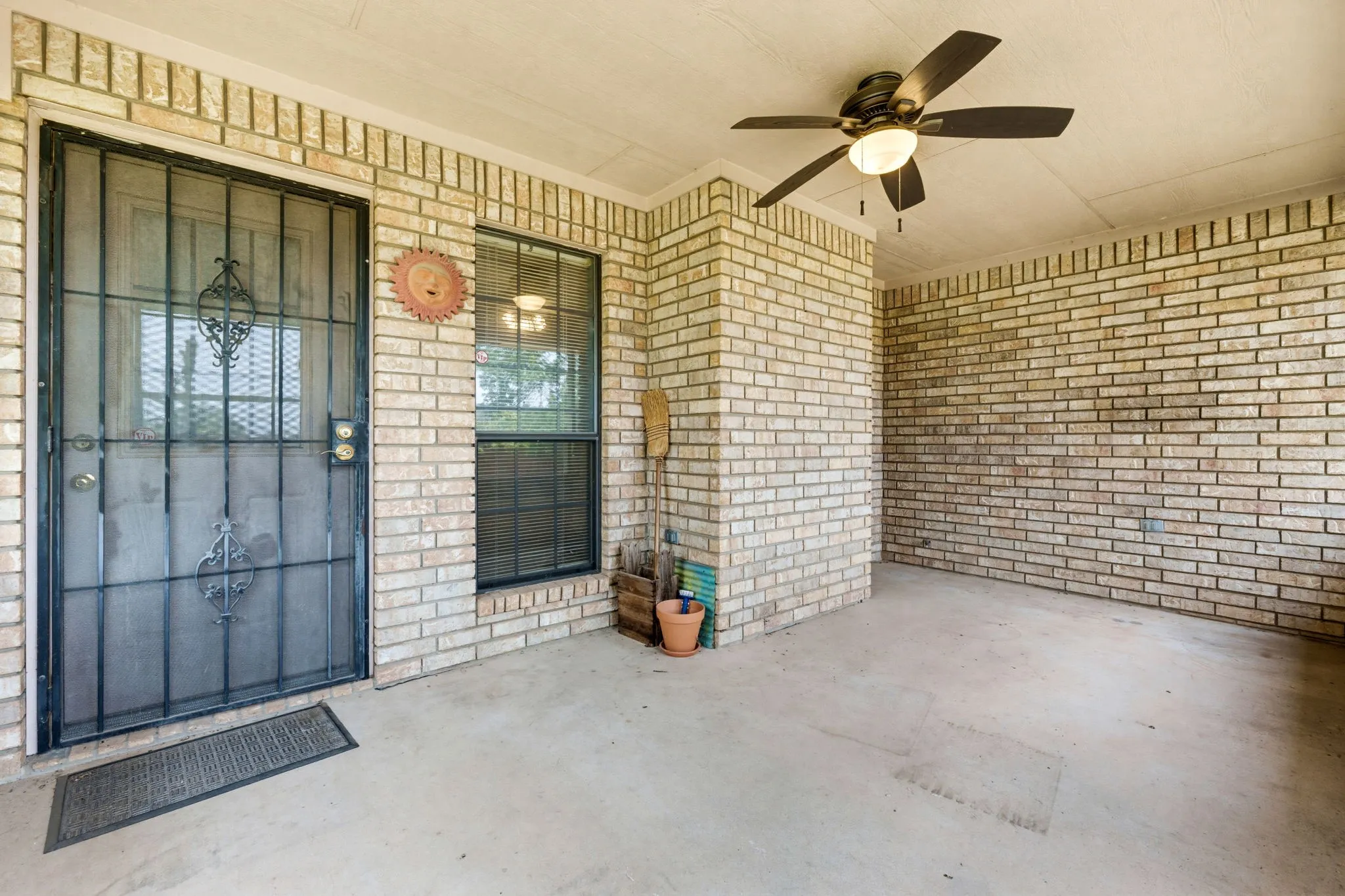 Covered concrete patio with brick walls, a ceiling fan with integrated lighting, and a security screen door
