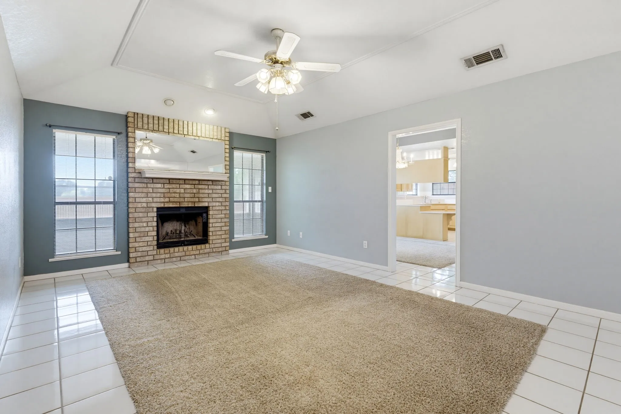 Vaulted ceiling with an integrated ceiling fan, brick fireplace with mantel, and tile flooring