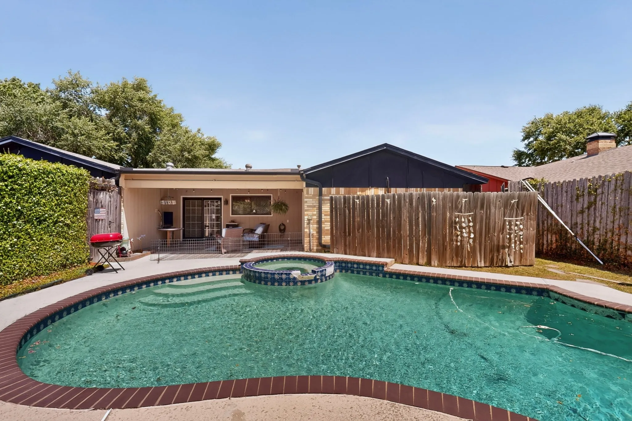 Private backyard oasis featuring a freeform swimming pool with integrated spa and brick coping, a covered patio, and mature perimeter landscaping