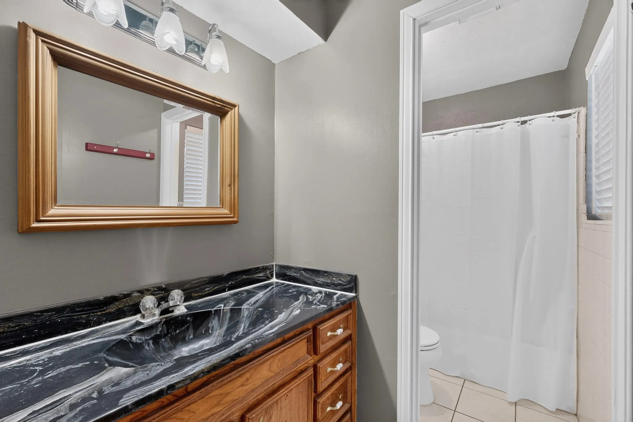 Bathroom vanity with dark veined countertop, wood-finish cabinetry, and a framed mirror