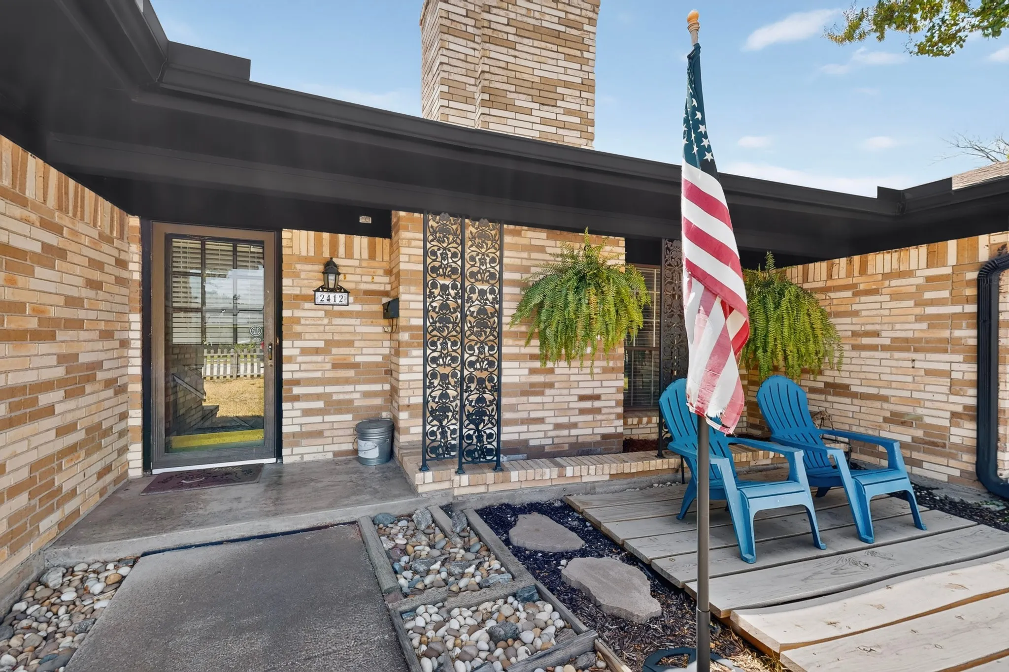 Brick exterior with a dark-colored fascia, featuring a concrete entry path, a decorative metal screen door, and exterior sconce lighting
