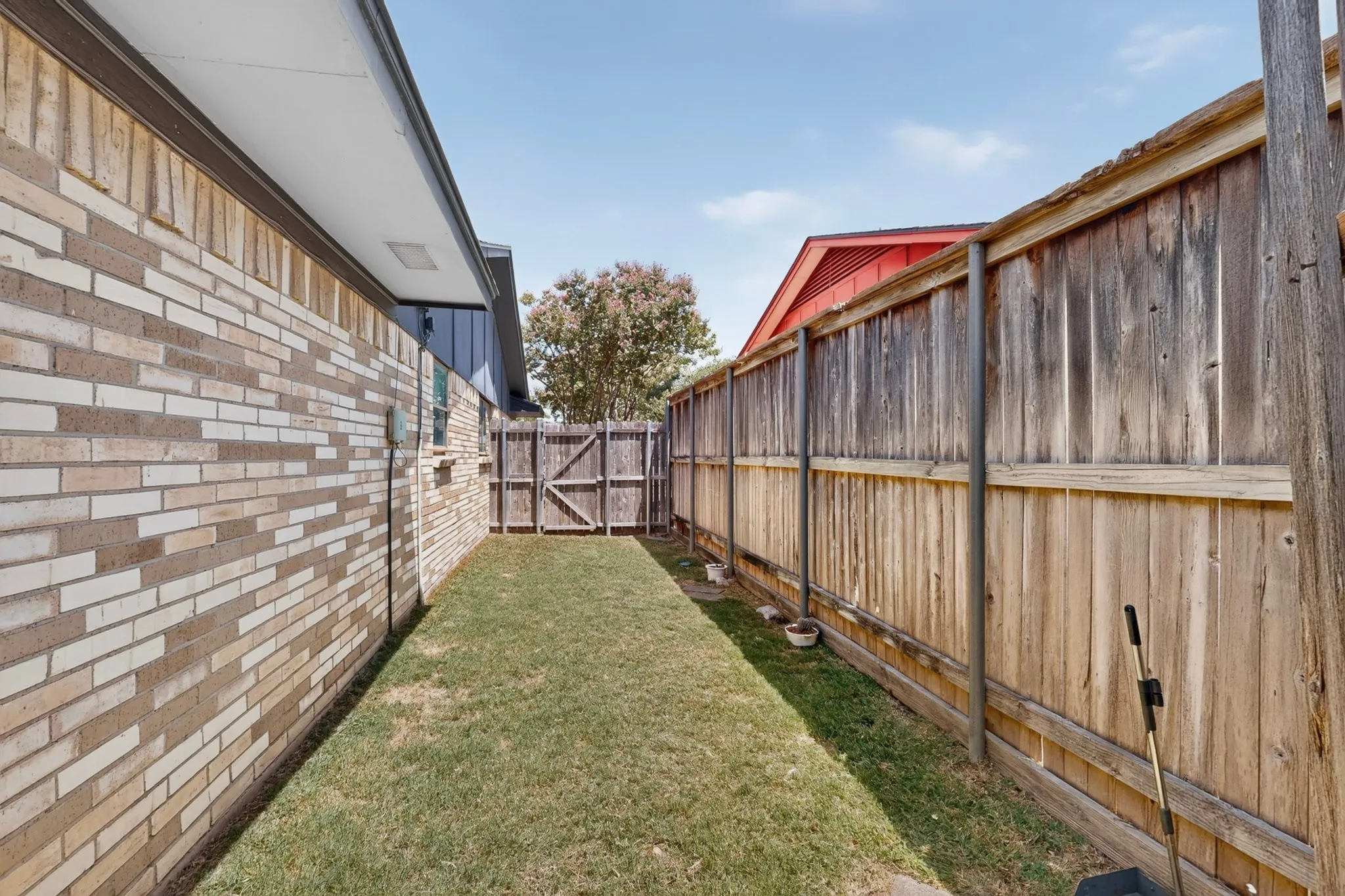 Spacious side yard featuring a manicured lawn, wood-constructed fencing with horizontal detailing, and brick exterior with mixed-tone finishes