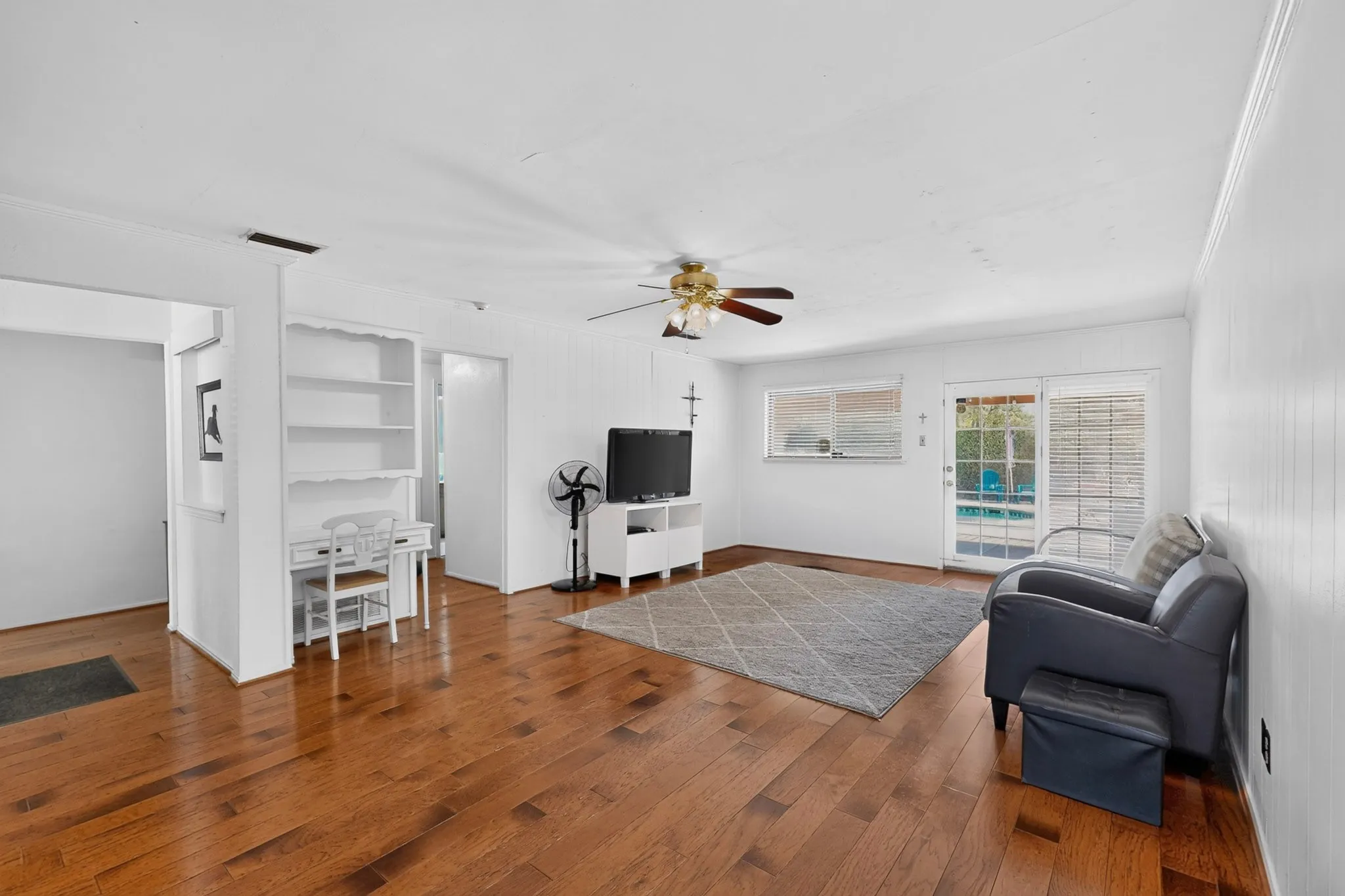 Hardwood flooring, white paneled walls, built-in shelving, ceiling fan, and glass door