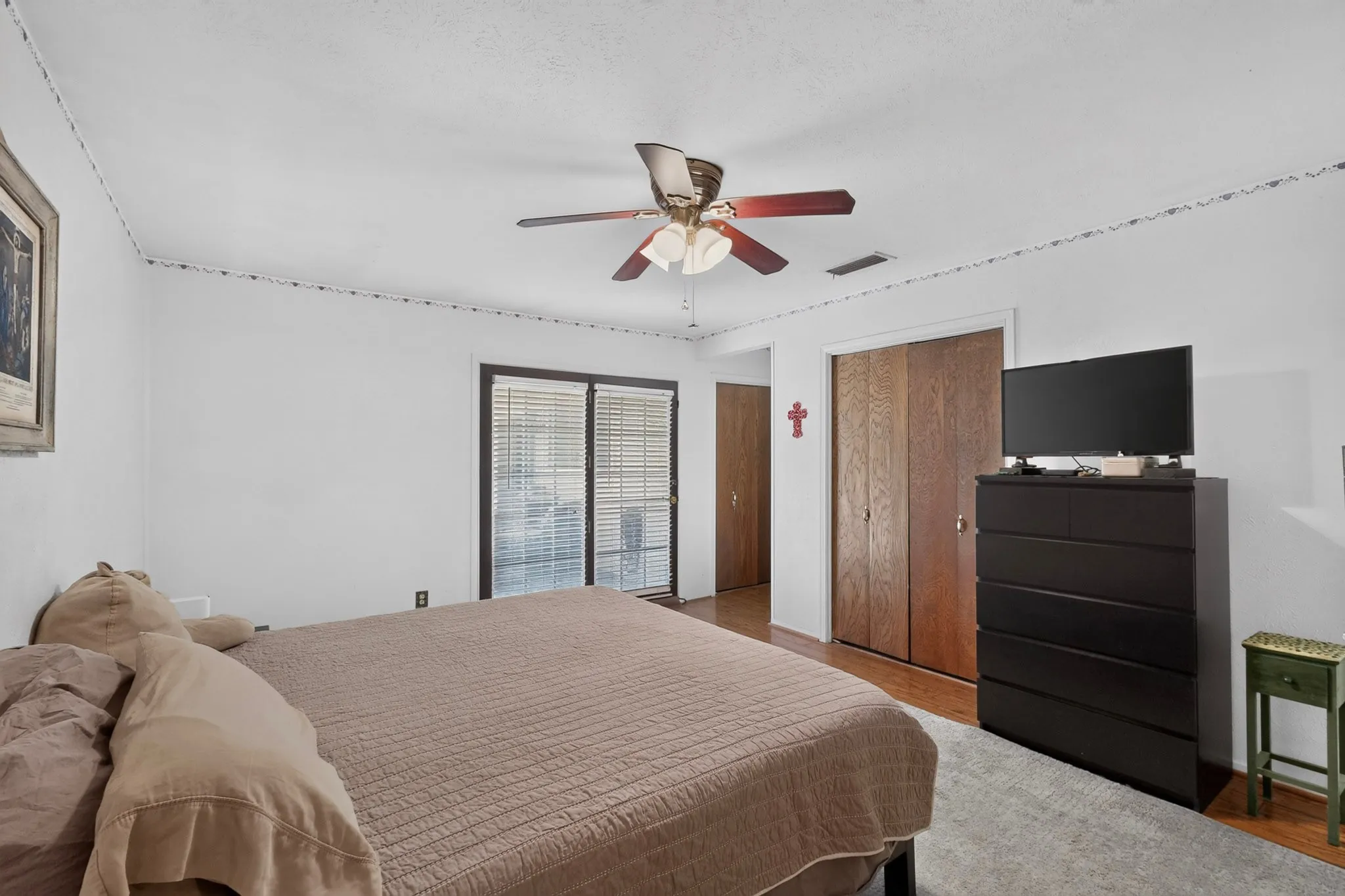 Sliding glass doors, wood-finish flooring, ceiling fan with integrated lighting, and bi-fold closet doors