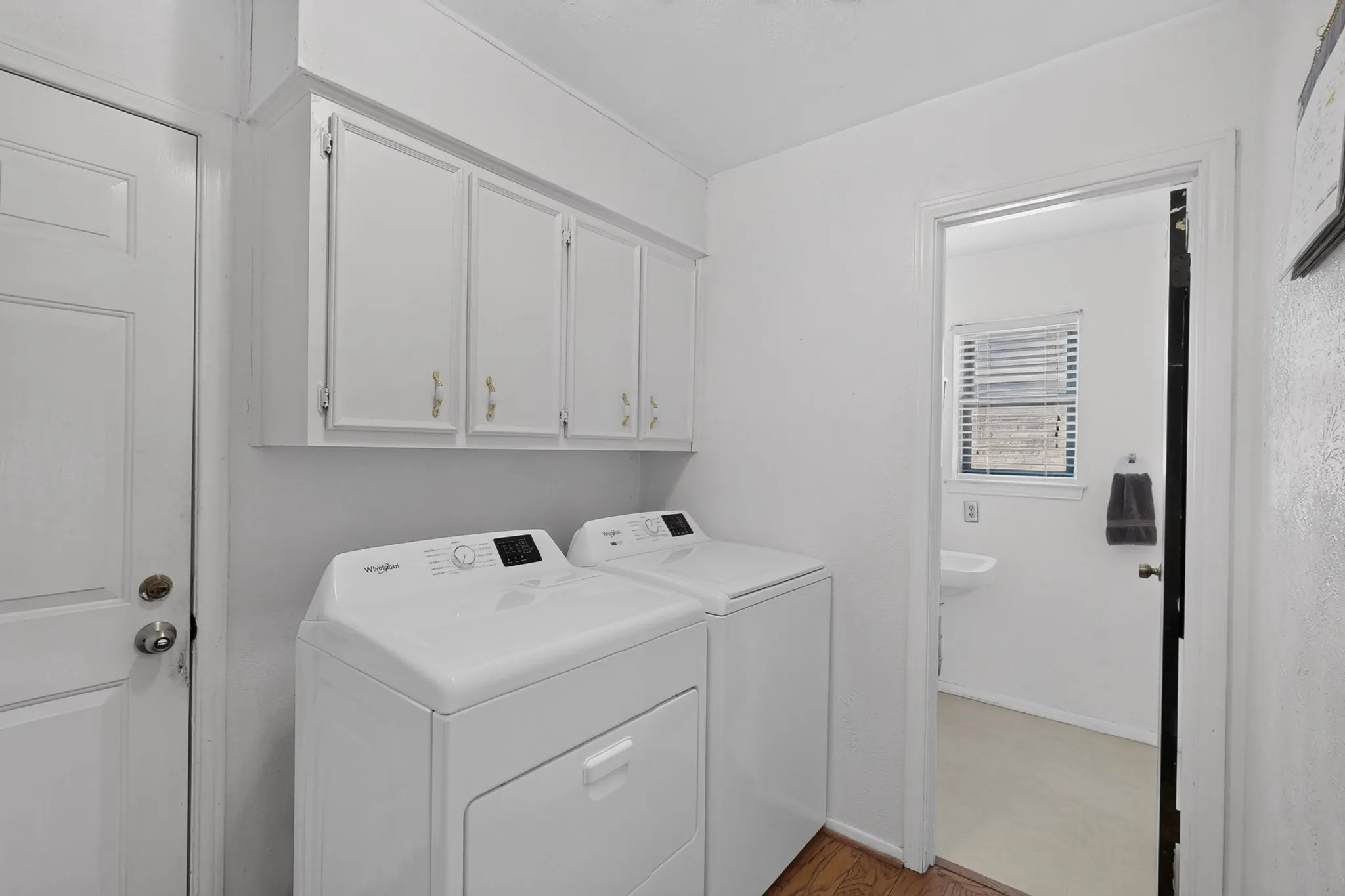 Dedicated laundry room featuring side-by-side washer and dryer appliances, ample cabinetry storage with overhead shelving, wood-finish flooring, and bright, neutral finishes throughout