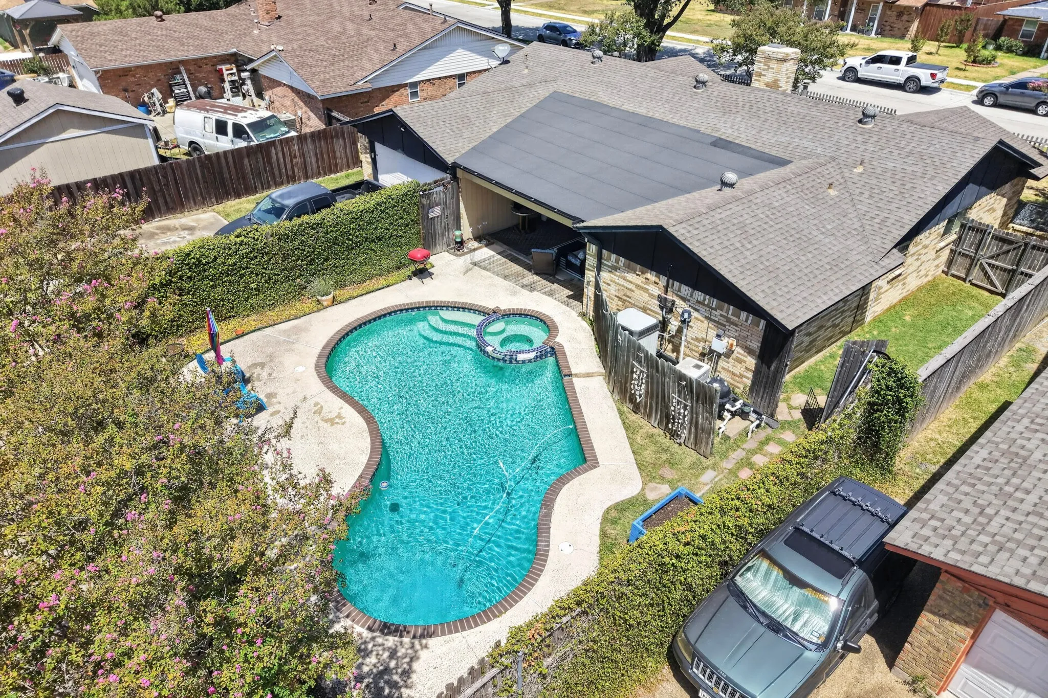 Rear exterior featuring a shaped swimming pool with integrated spa and steps, a covered patio area, and mature landscaping