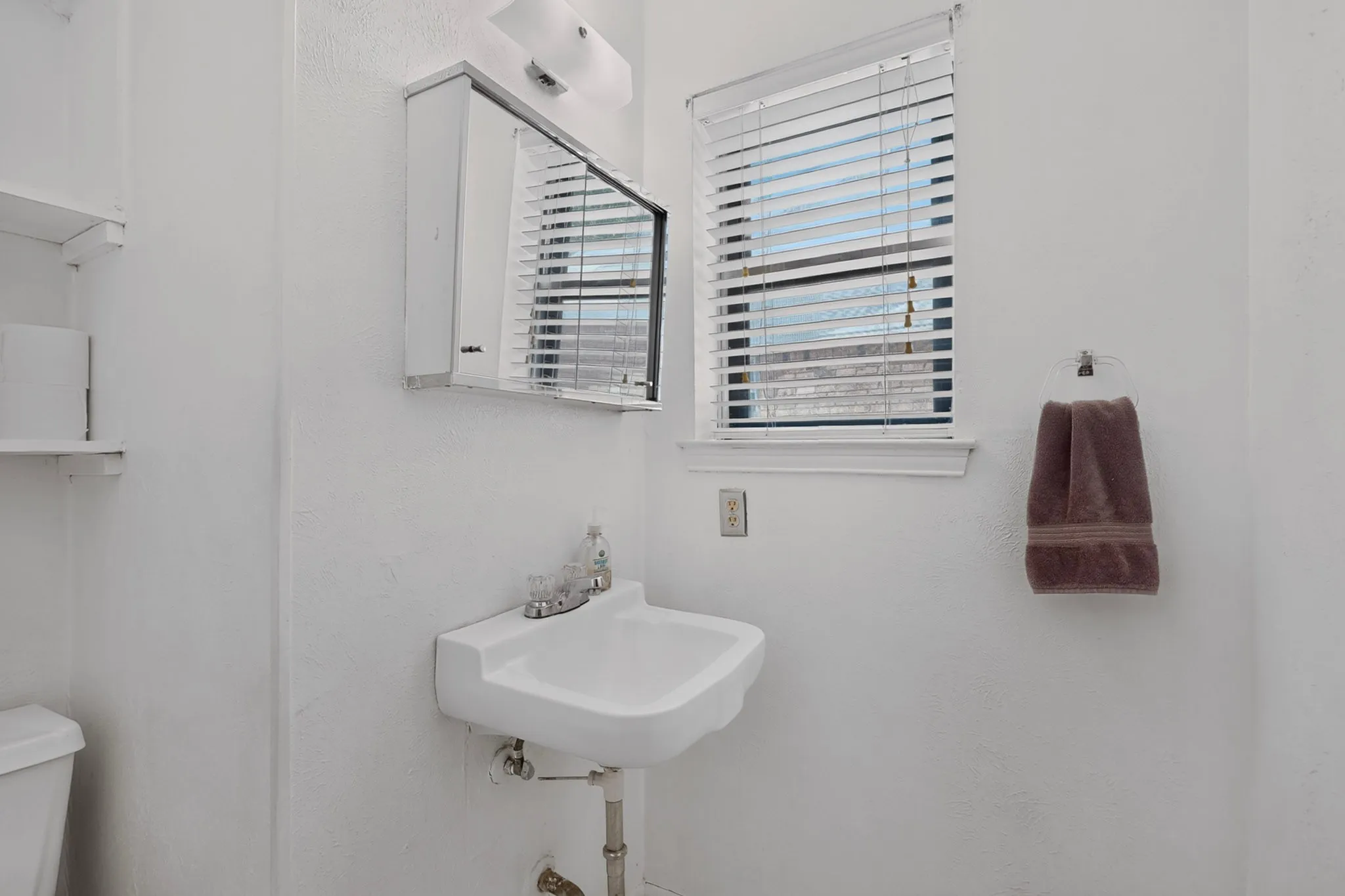  1/2 bath with Wall-mounted sink with chrome faucet, built-in medicine cabinet, window with blinds, and wall-mounted towel ring