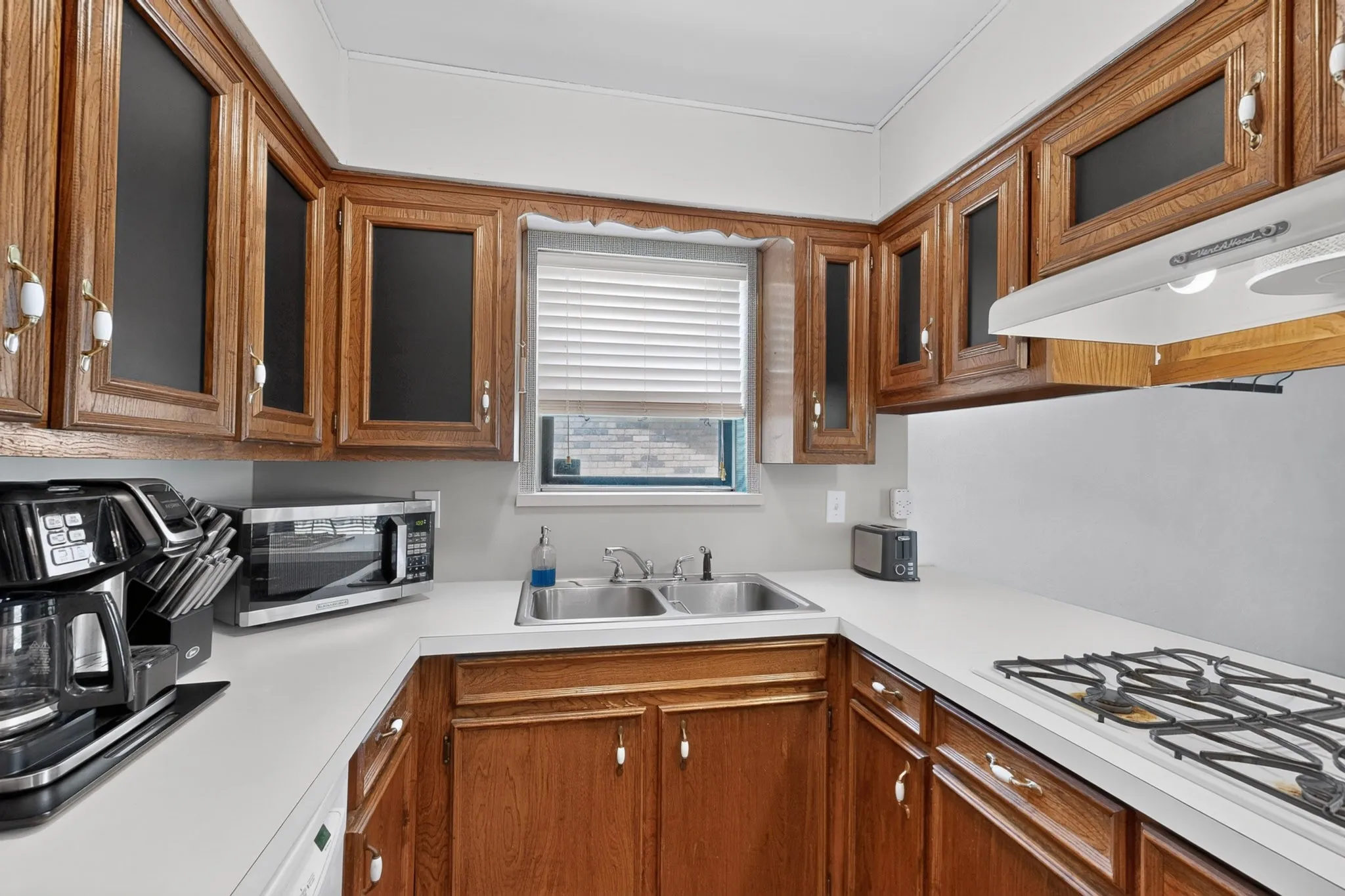 U-shaped kitchen with wood cabinetry, white countertops, and a dual basin stainless steel sink