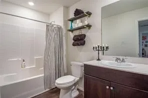 Full bathroom featuring a white tub and shower combination with subway tile surround, dark wood-finish vanity with an integrated sink, and an expansive wall-mounted mirror