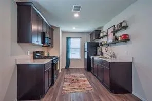 Galley kitchen with dark wood-finish cabinetry, light-toned countertops, and wood-finish flooring