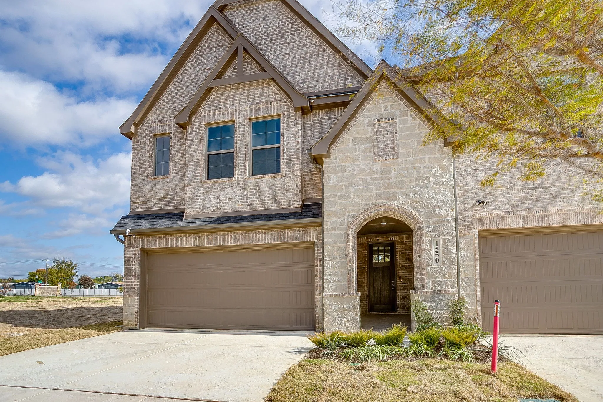 View of front of property featuring brick siding, a garage, driveway, a shingled roof, and stone siding
