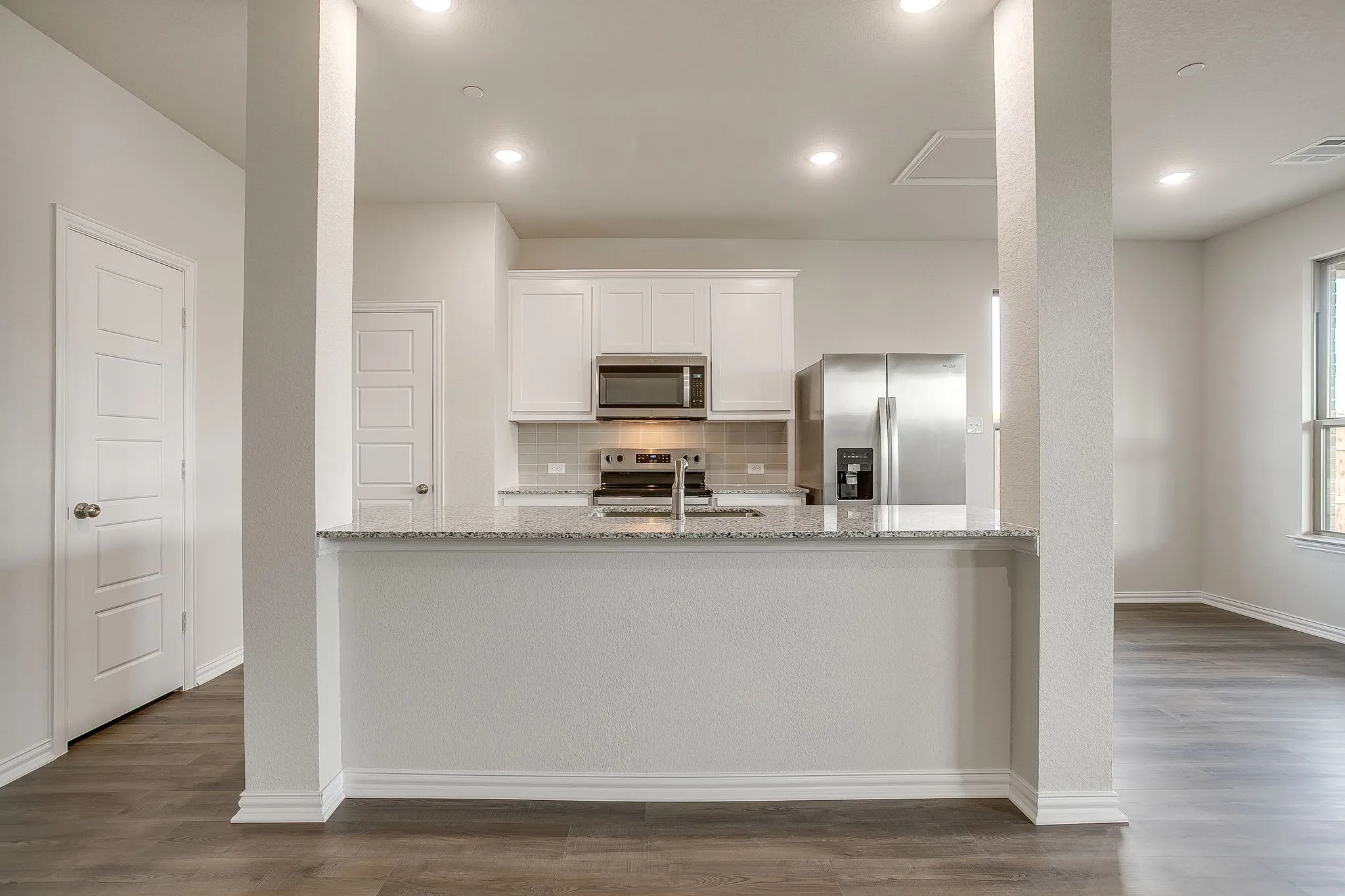 Kitchen with light stone countertops, white cabinets, decorative backsplash, stainless steel appliances, and dark wood-type flooring