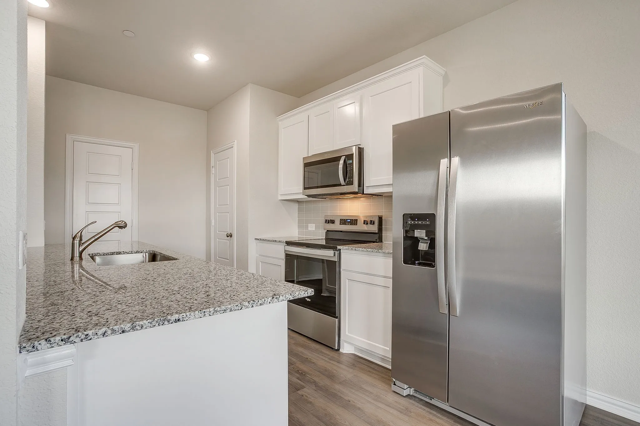 Kitchen with appliances with stainless steel finishes, light stone counters, white cabinets, backsplash, and dark wood-type flooring