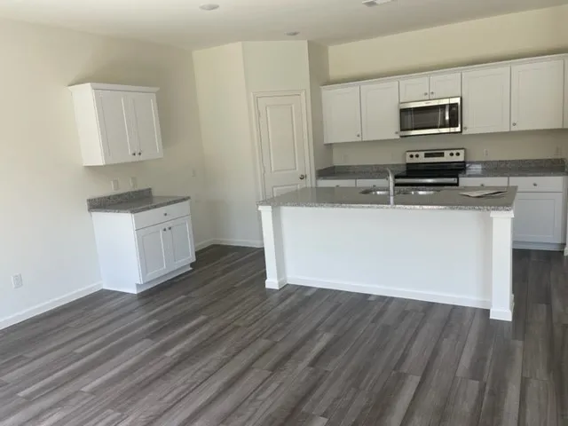 Modern kitchen featuring white cabinetry, stainless steel appliances including a built-in microwave, gray quartz countertops, and a large center island with white base cabinetry