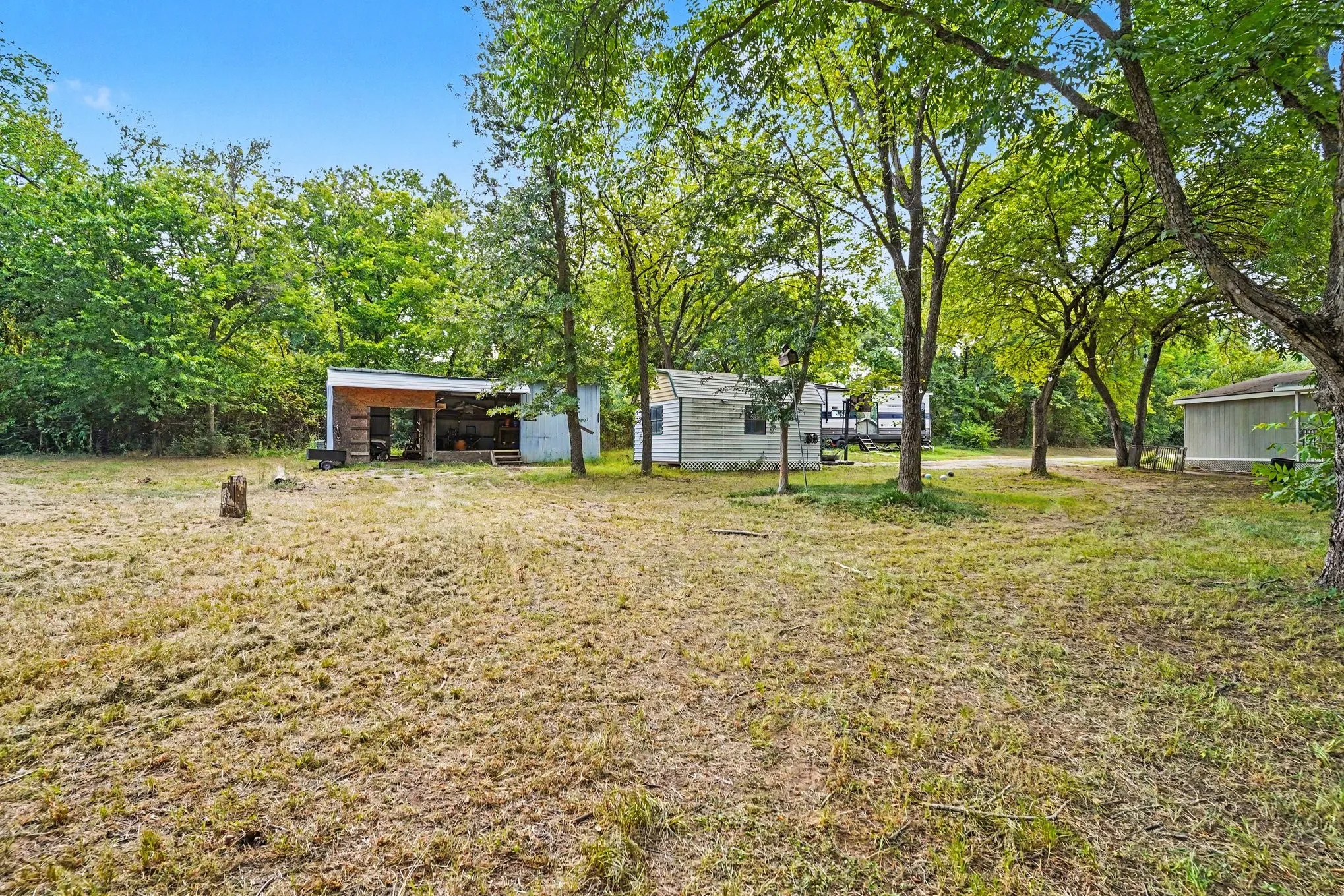 Expansive outdoor space featuring several mature trees and multiple outbuildings