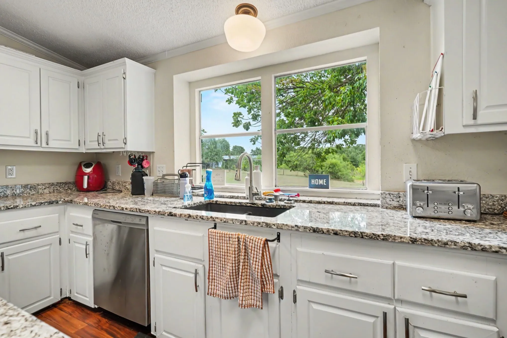 Bright, updated kitchen showcasing crisp white cabinetry with brushed nickel hardware, granite-style speckled countertops, and stainless steel appliances