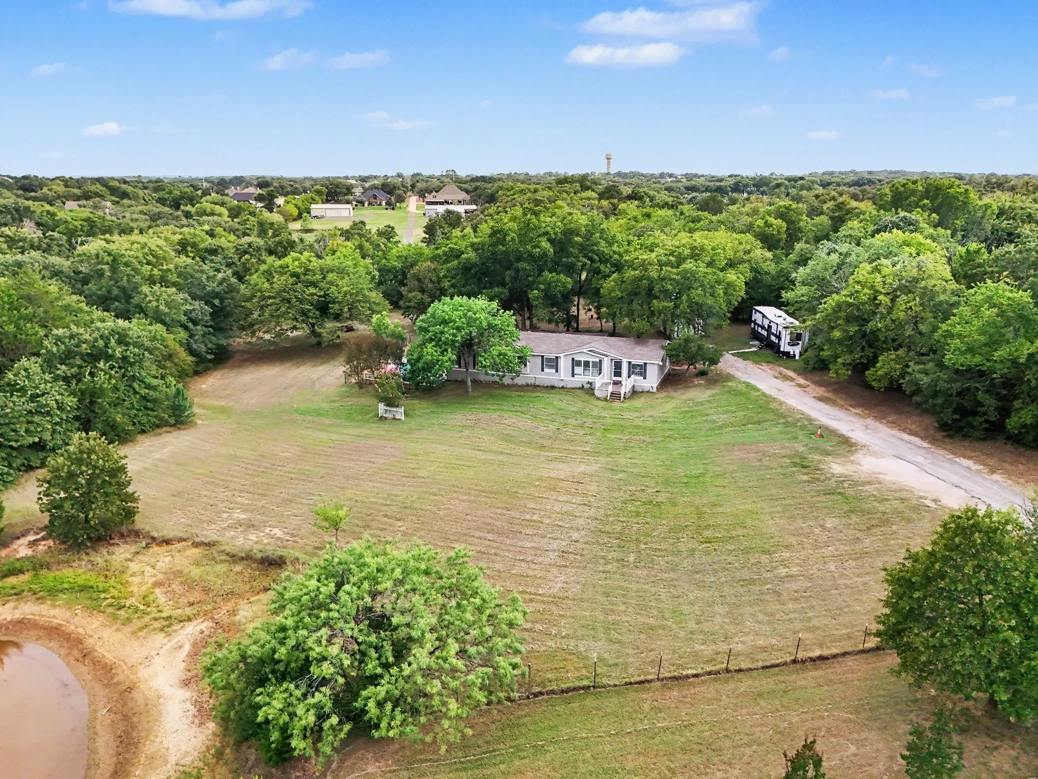 Spacious rural property featuring a single-story residence, expansive cleared areas, a private pond, and mature tree coverage