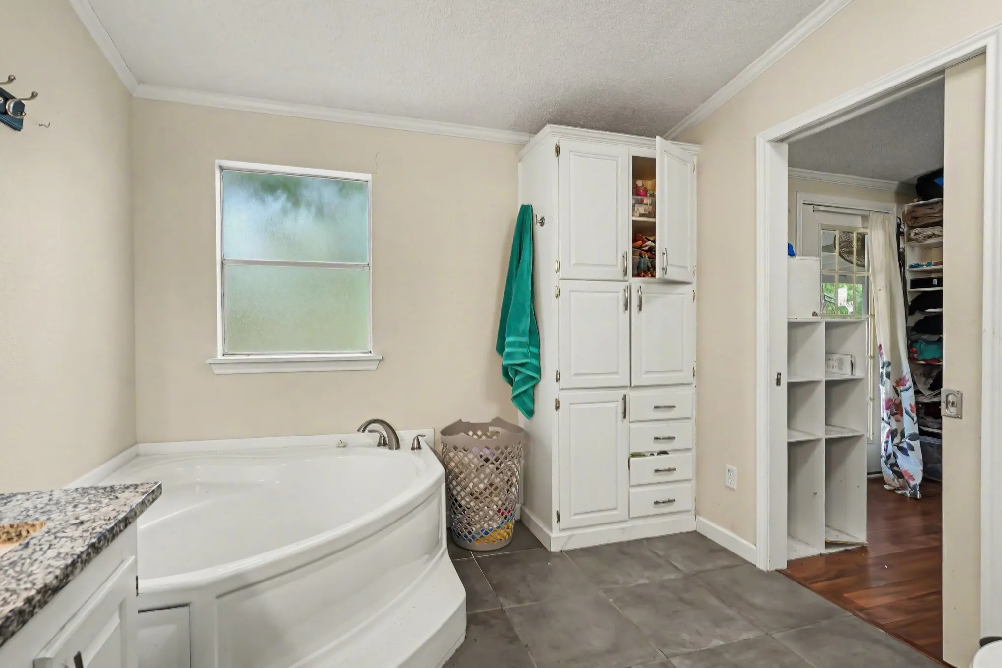 Soaking tub with brushed nickel fixtures, granite-finish vanity countertop, white built-in storage cabinetry, and gray floor tiles