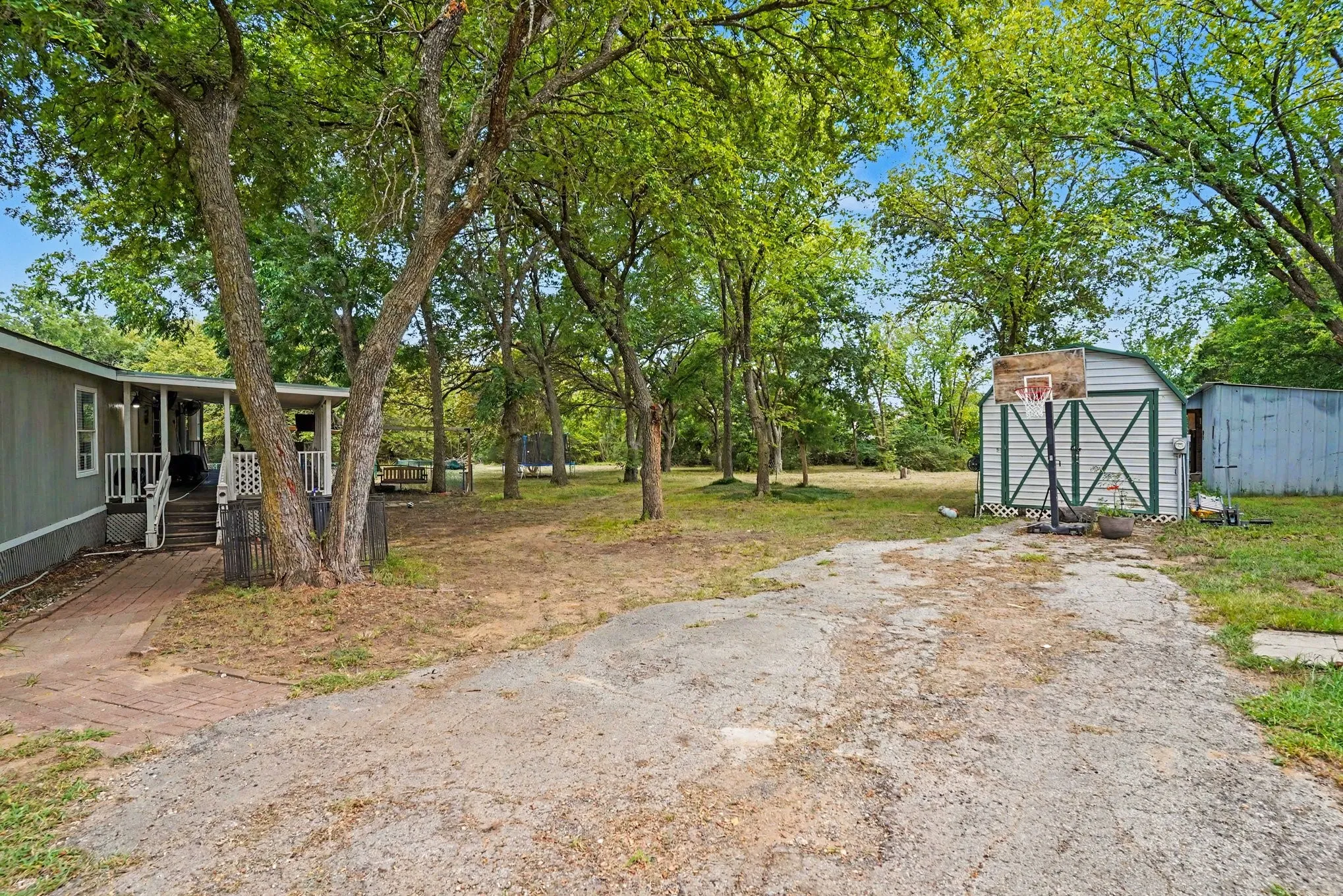 Spacious grounds featuring mature shade trees, gravel driveway, and detached outbuildings