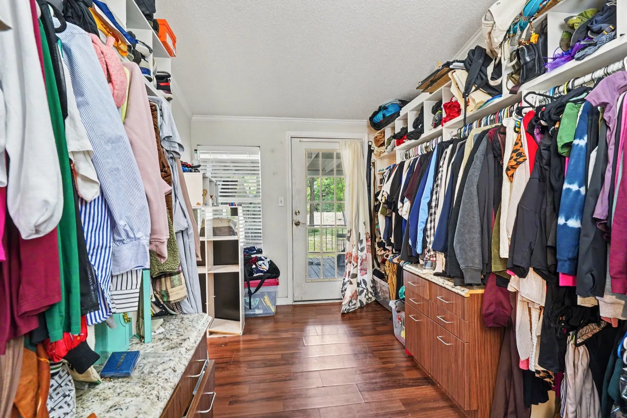 Walk-in closet featuring wood-finish flooring, built-in shelving, integrated hanging rods, a French door, and a built-in dresser with a stone countertop