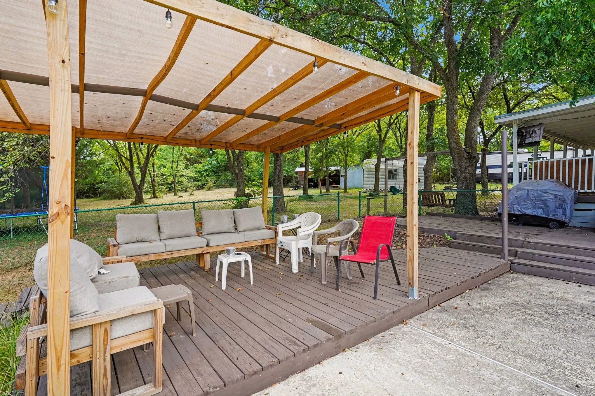 Spacious covered deck with wood-finish flooring and timber beam construction, featuring comfortable seating areas, multiple accent chairs, and ample shade