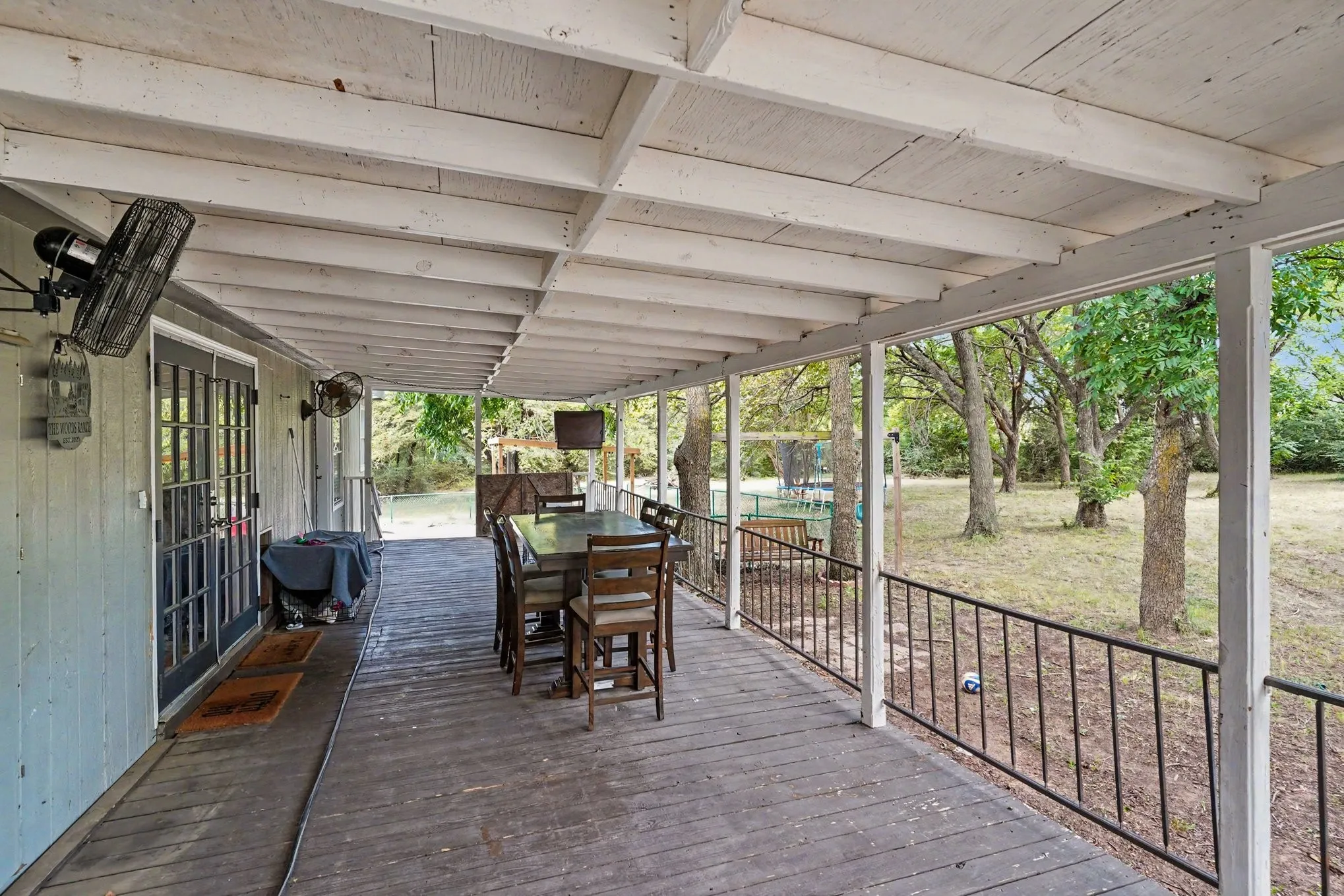 Expansive covered porch featuring a wood-finish floor, white exposed beam ceiling, and a black metal railing